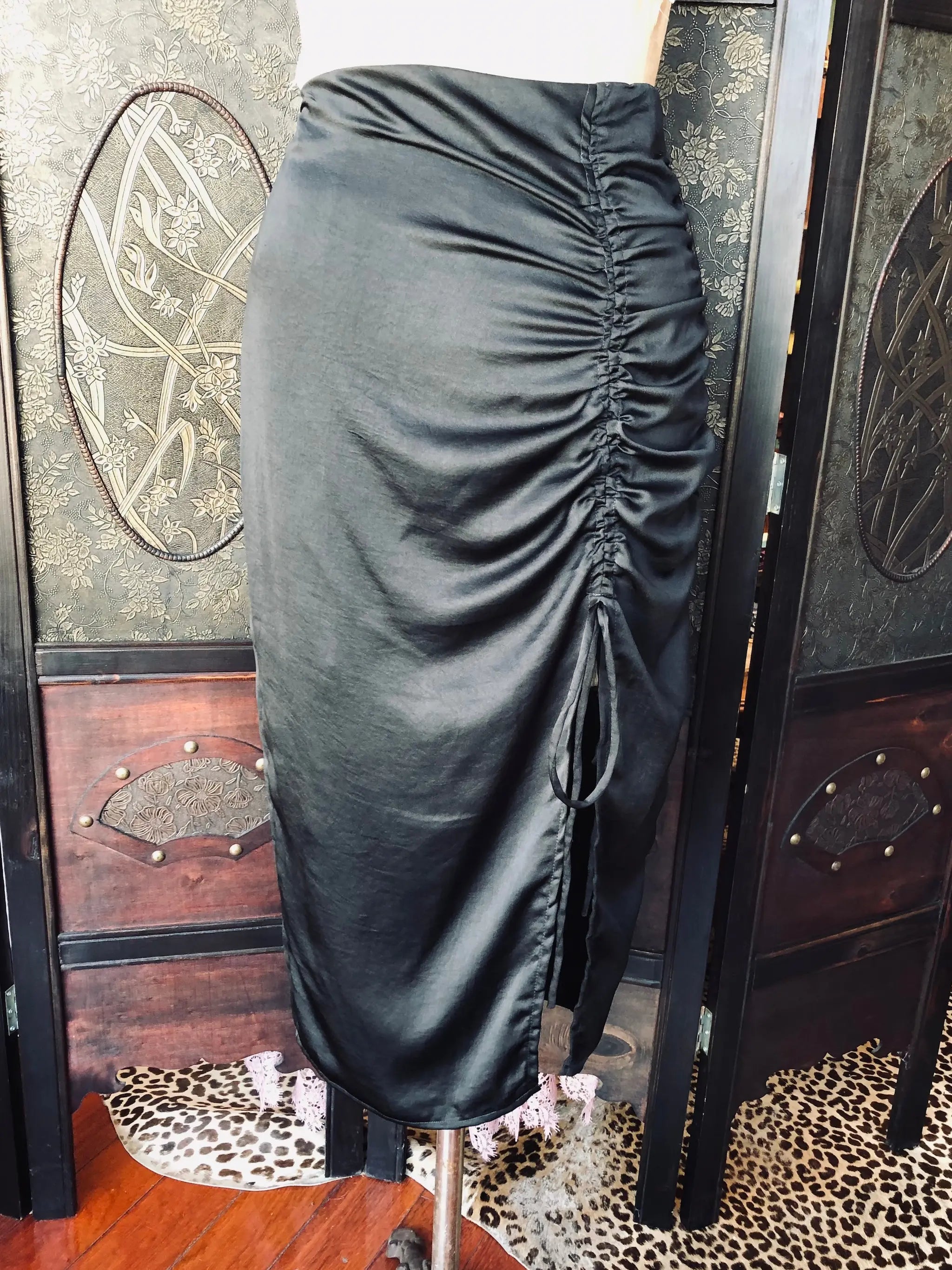 Broochella Kookai Black satin skirt on a mannequin against a decorative wall.