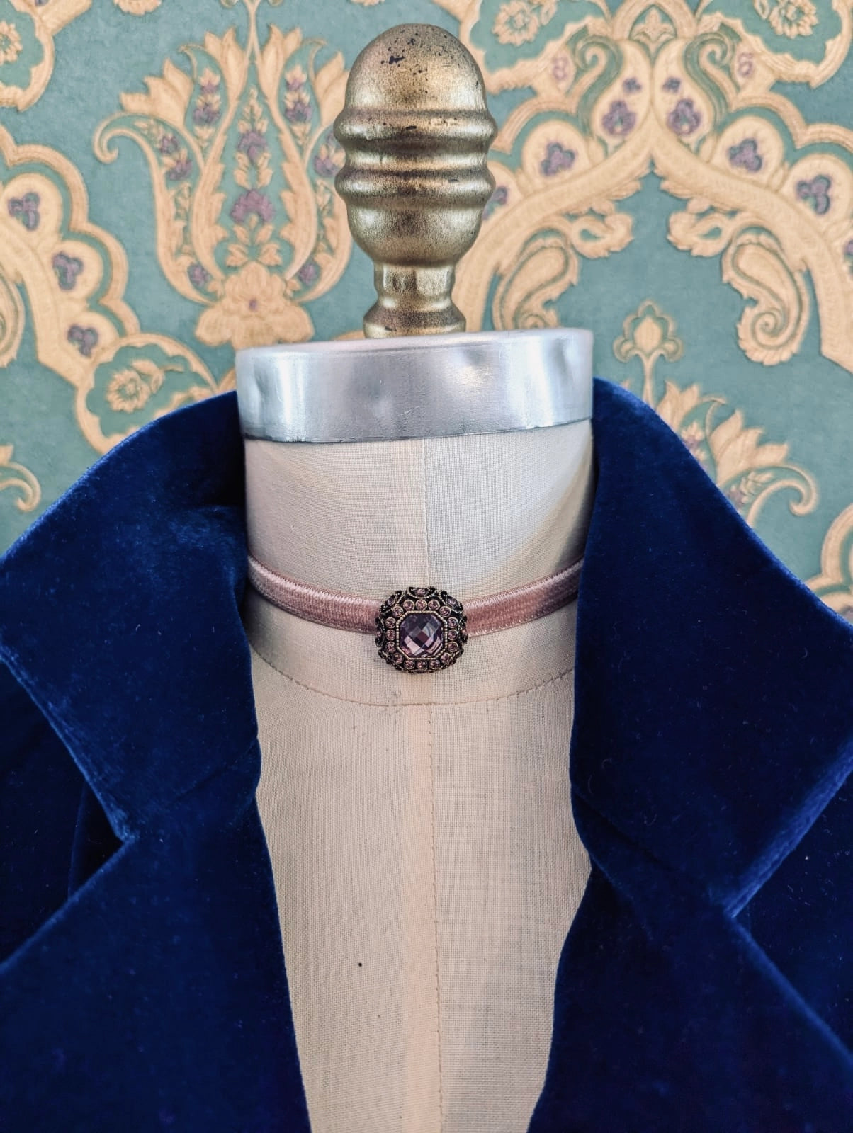 Broochella blush pink lady whistledown velvet choker with crystal embellishment.  Pictured on a mannequin.  The background is green and gold damask wallpaper
