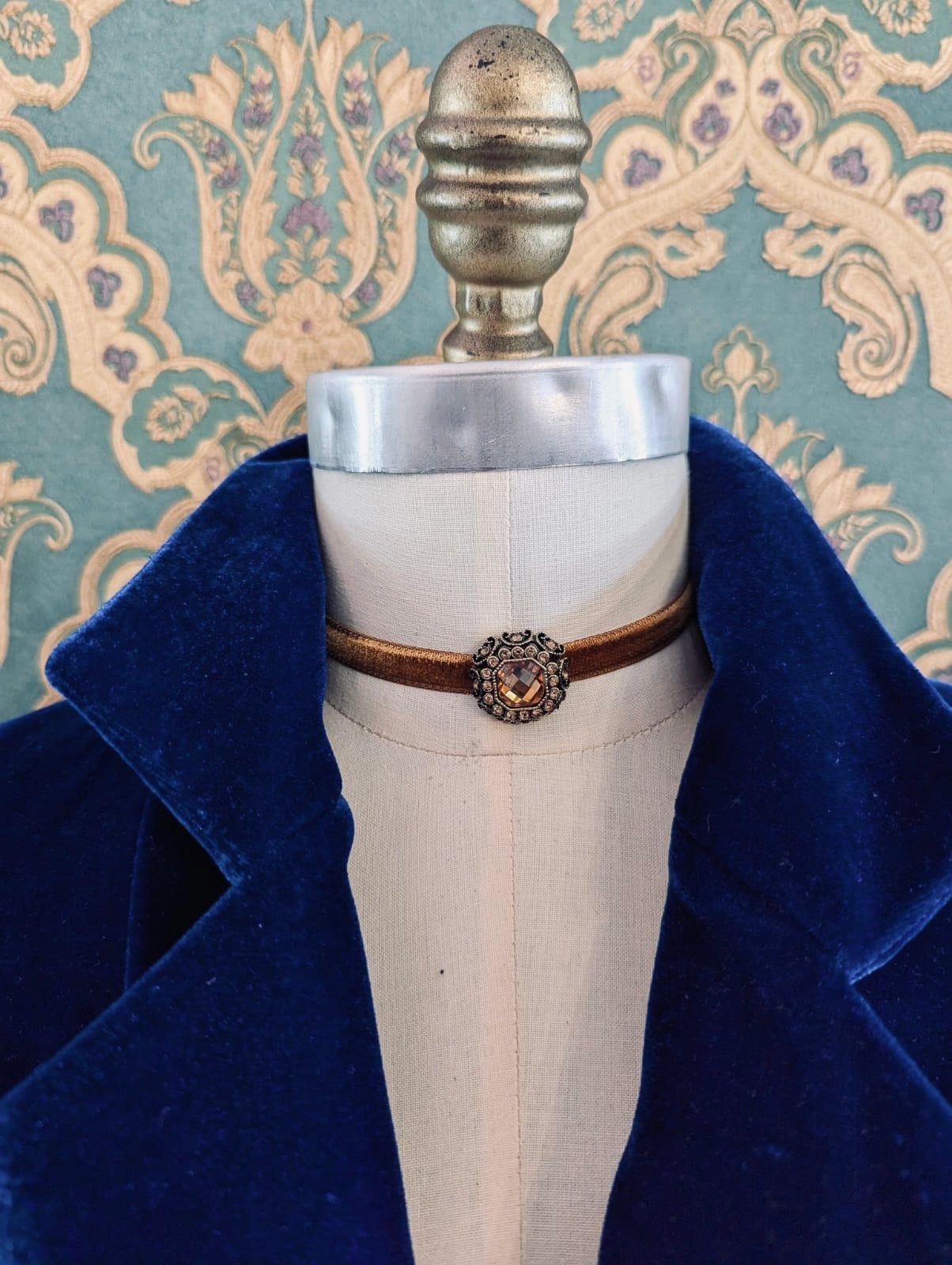 Broochella bronze lady whistledown velvet choker with crystal embellishment.  Pictured on a mannequin.  The background is green and gold damask wallpaper