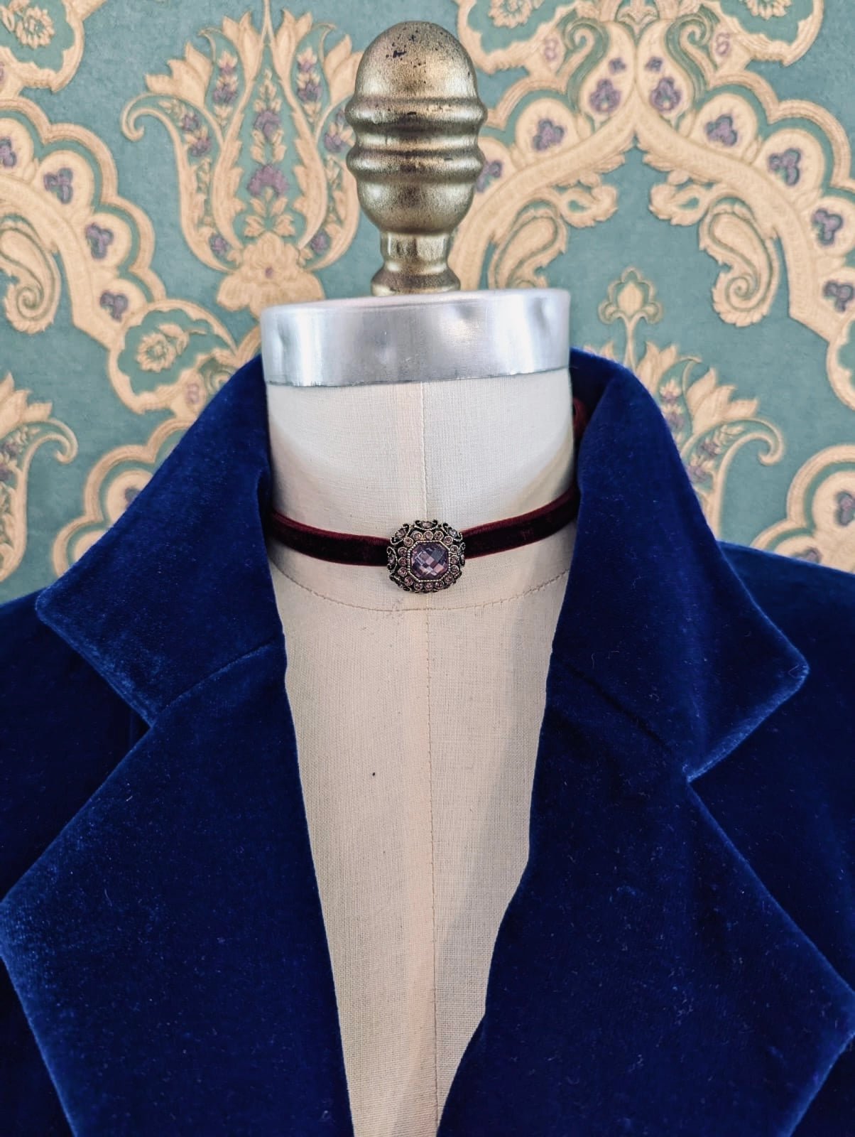 Broochella burgundy lady whistledown velvet choker with crystal embellishment.  Pictured on a mannequin.  The background is green and gold damask wallpaper
