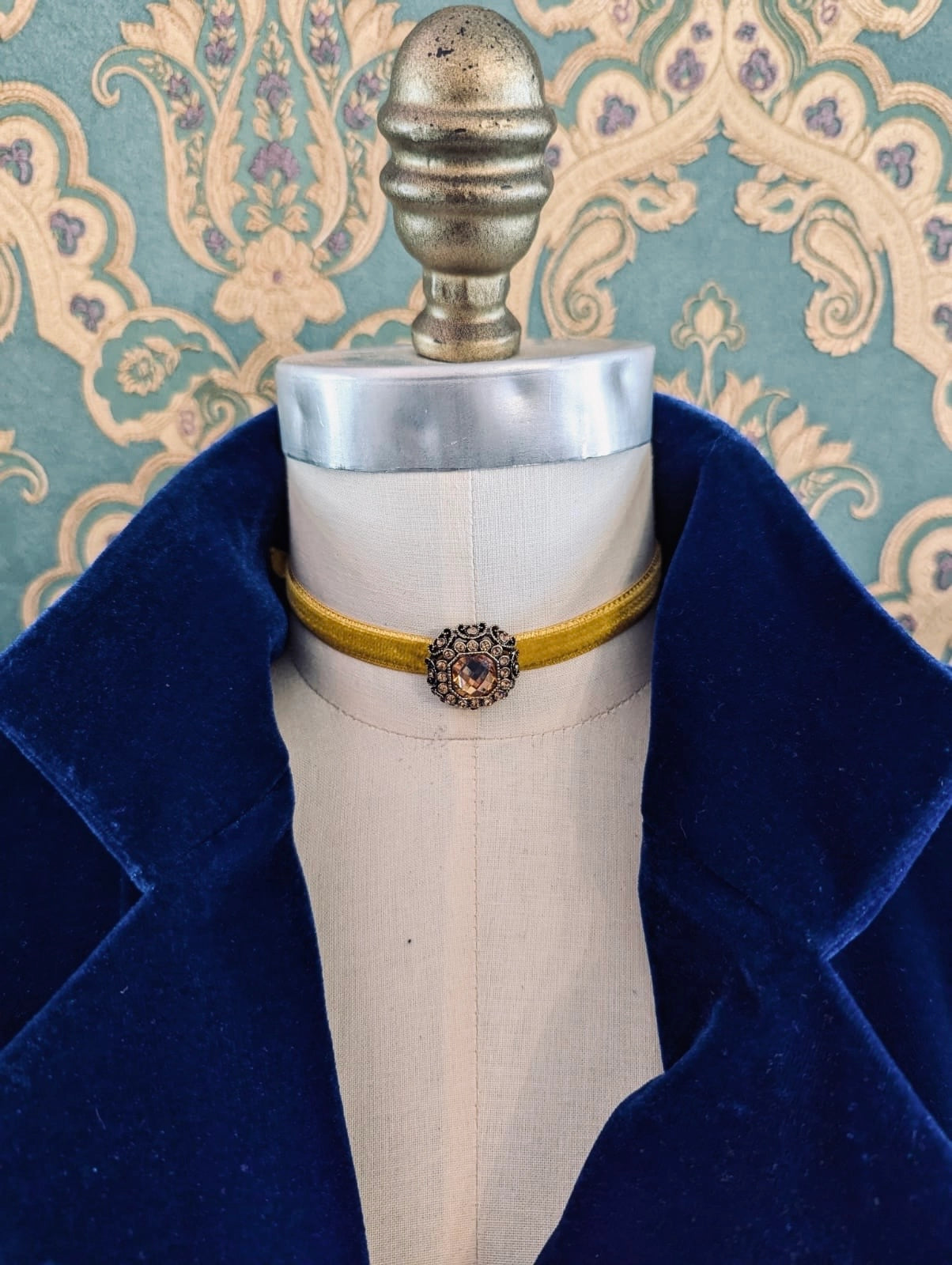Broochella gold lady whistledown velvet choker with crystal embellishment.  Pictured on a mannequin.  The background is green and gold damask wallpaper
