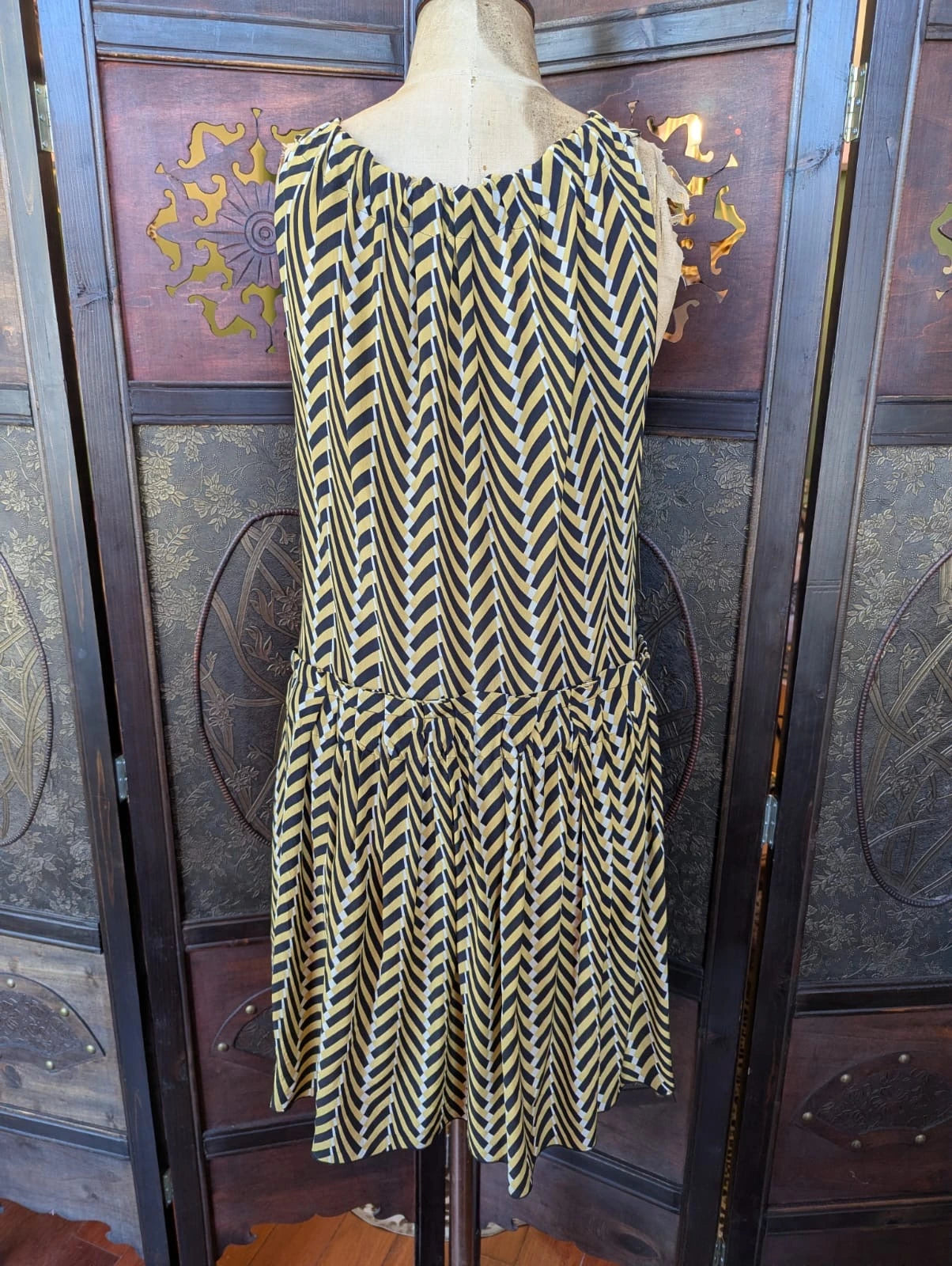Broochella The Stylist's Closet Lanvin authentic designer silk dress in black and gold chevron pattern viewed form the back. It is pictured on a vintage mannequin. The background is an ornate dark wood room divider