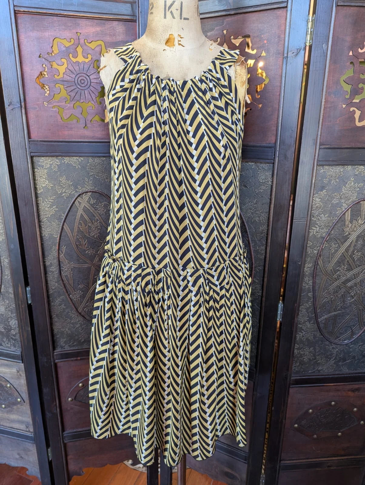 Broochella The Stylist's Closet Lanvin authentic designer silk dress in black and gold chevron pattern. It is pictured on a vintage mannequin. The background is an ornate dark wood room divider