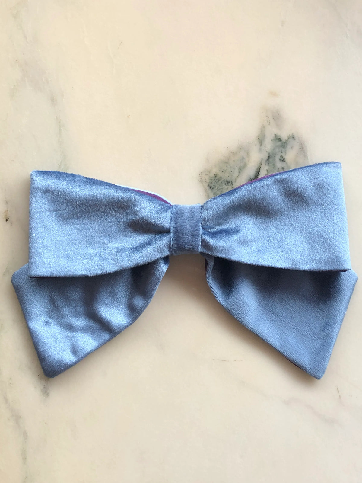 Broochella handmade Large Velvet Bow Brooch in soft blue velvet with contrasting purple edging, featuring an oversized designer double bow with sculptural loops, photographed on white marble.