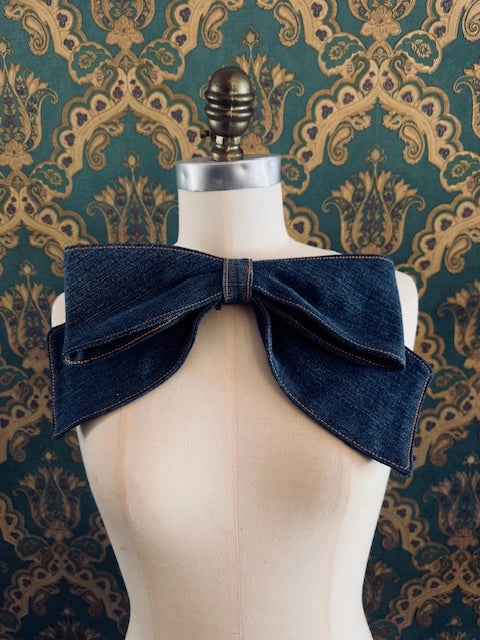 Broochella Large handmade denim bow brooch. Pictured on a mannequin. The background is green and gold damask wallpaper.