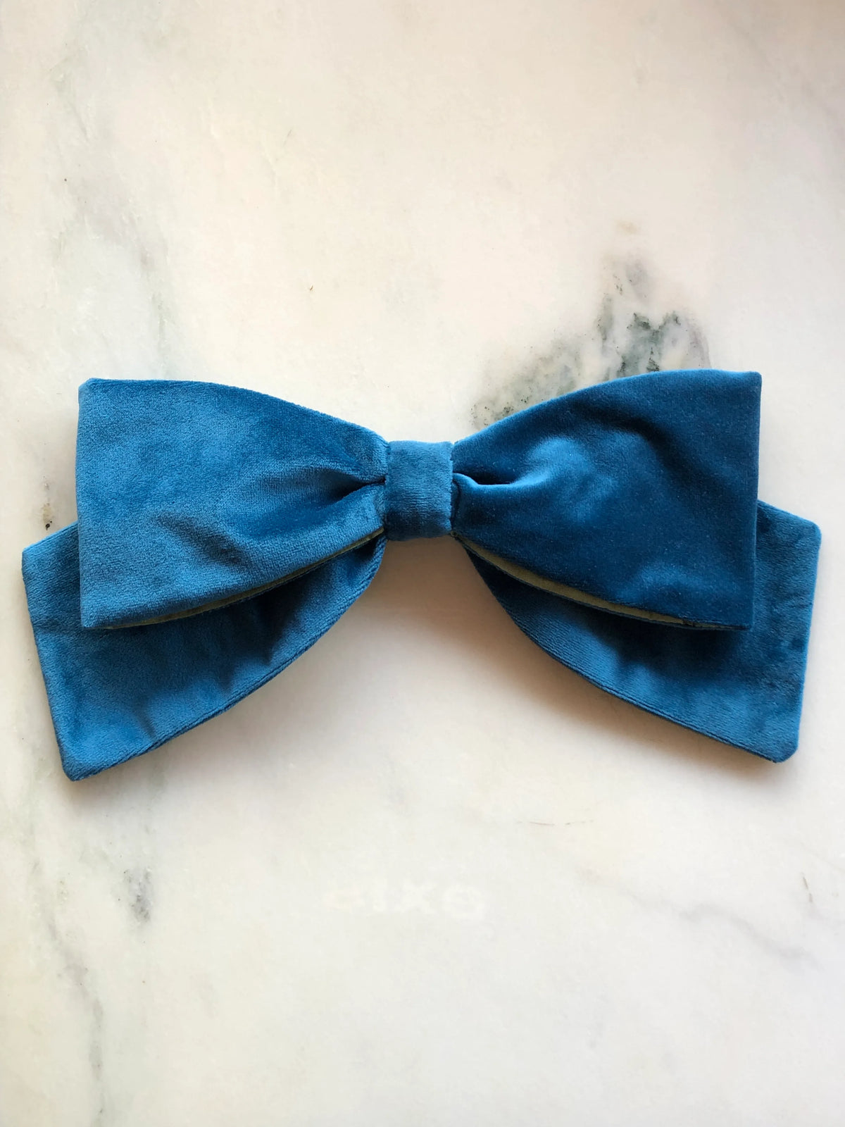 Broochella handmade Large Velvet Bow Brooch in rich peacock blue velvet with contrasting lime green lining, featuring an oversized designer double bow with sculptural loops, photographed on white marble.