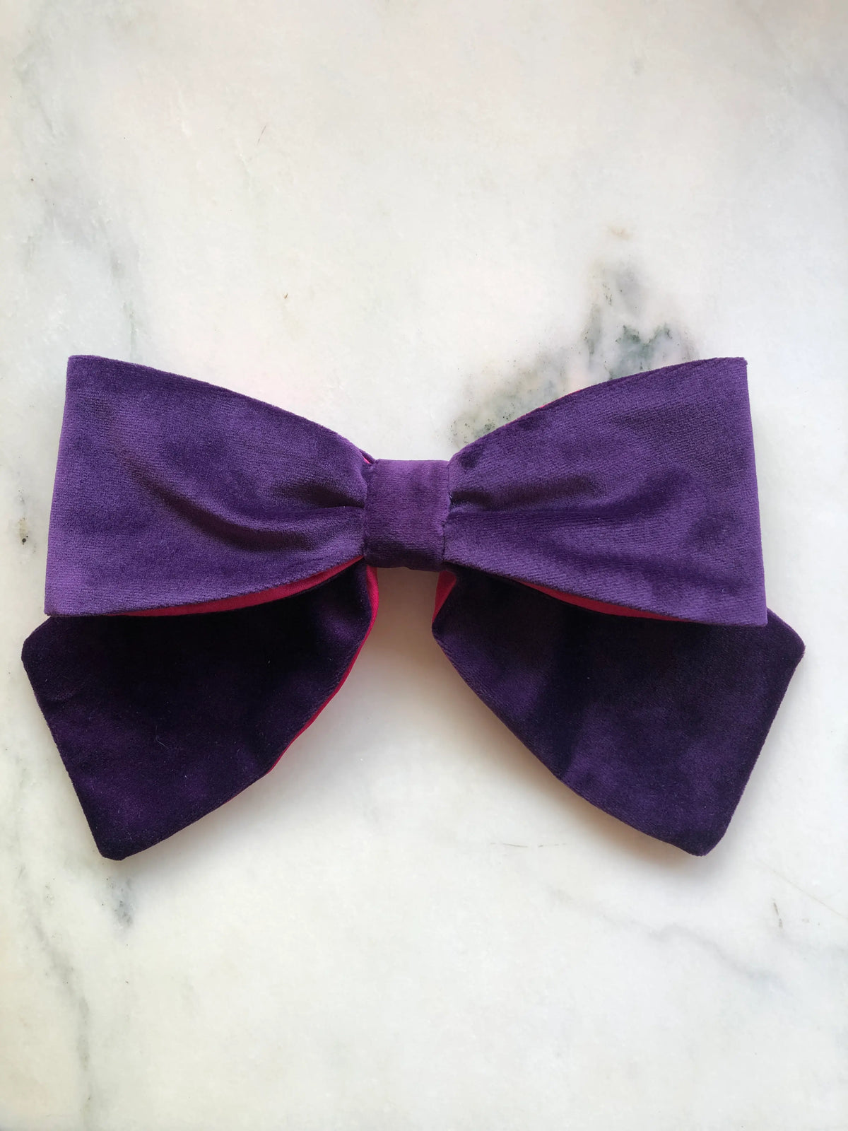 Broochella handmade Large Velvet Bow Brooch in deep purple velvet with contrasting vibrant fuchsia lining, featuring an oversized designer double bow with sculptural loops, photographed on white marble.
