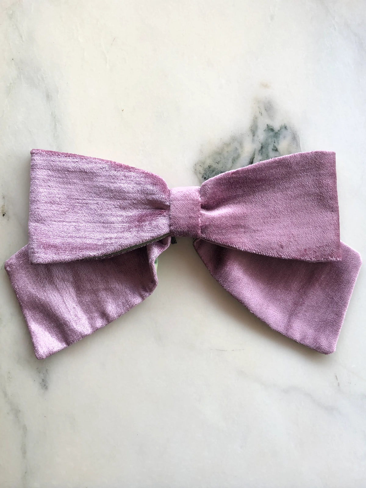 Broochella handmade Large Velvet Bow Brooch in soft violet velvet with contrasting green lining, featuring an oversized designer double bow with sculptural loops, photographed on white marble.