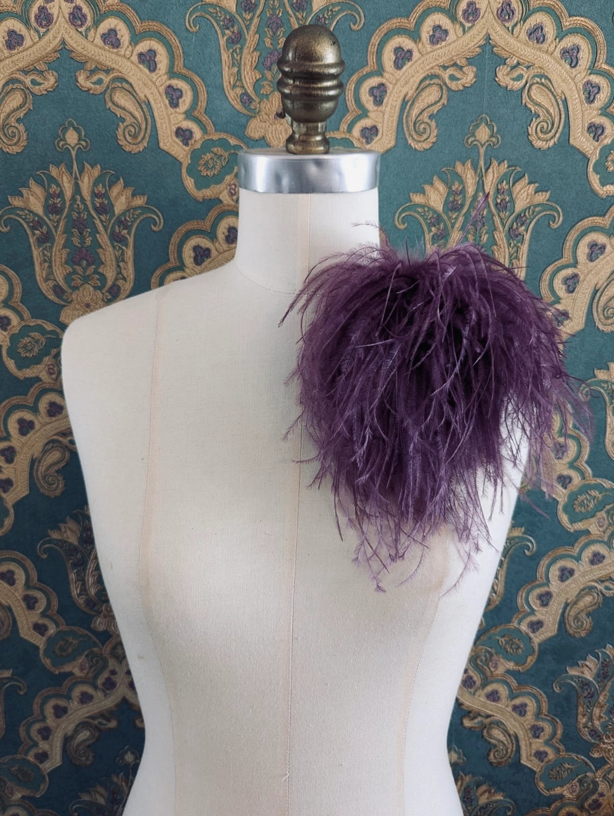 Broochella le pouffe handmade designer feather brooch in magenta.  It is pinned to a mannequin. The background is green and gold damask wallpaper