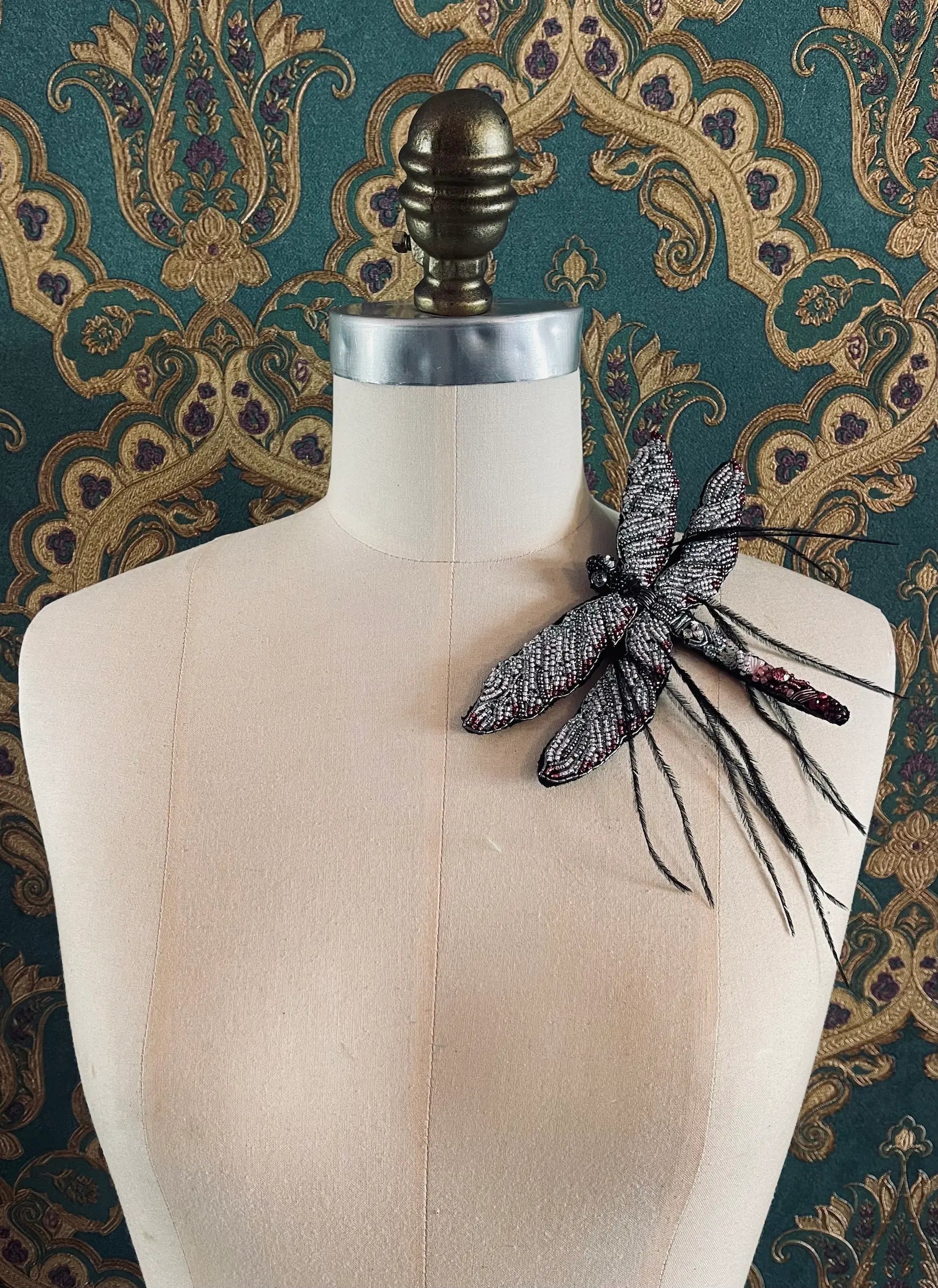 Broochella Libellula hand beaded black and pink dragonfly designer brooch. Pictured on a mannequin. The background is green and gold damask wallpaper