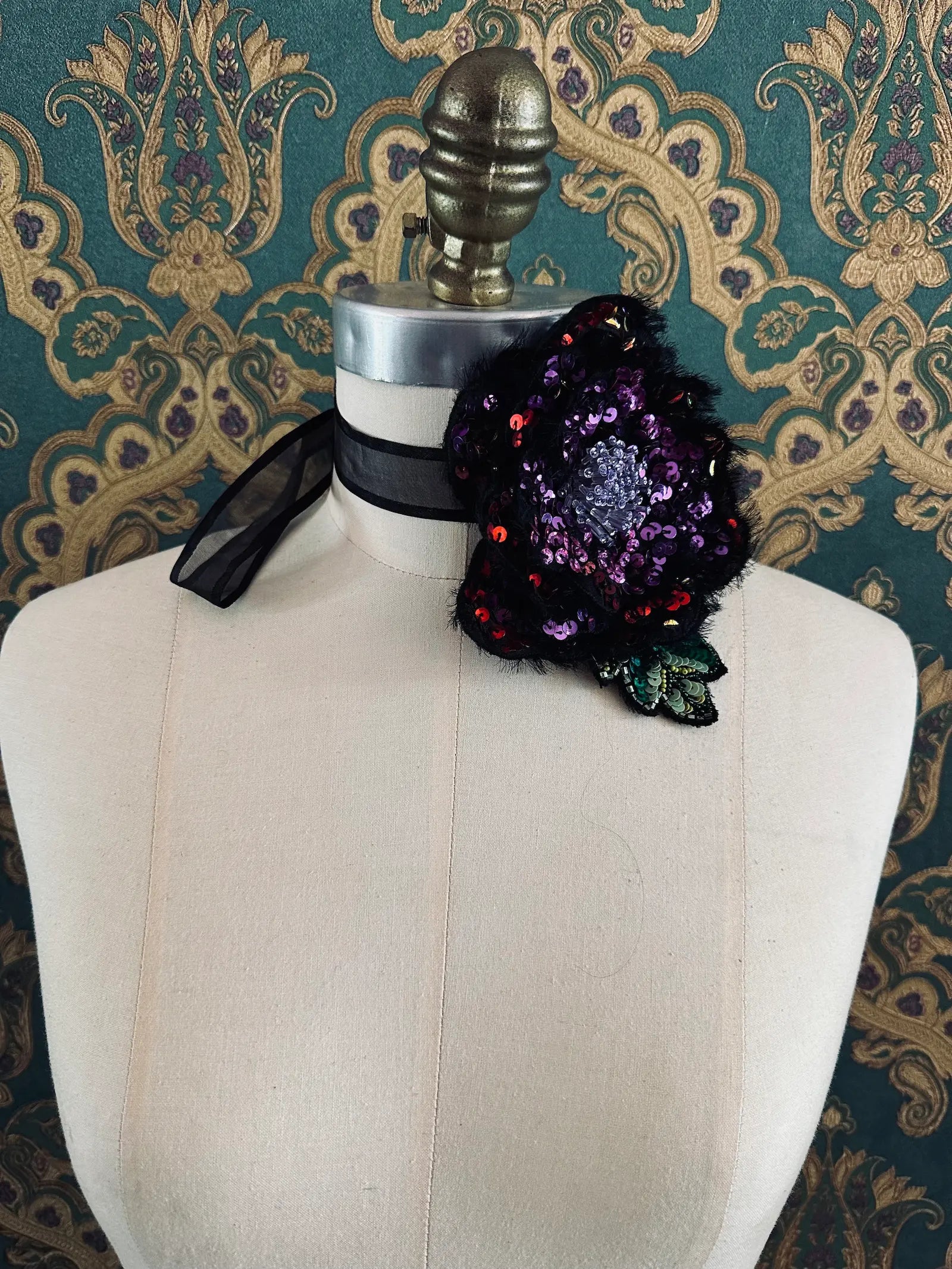 Broochella Luminosa hand beaded sequin choker and brooch in pink and black. Pictured on a mannequin. The background is green and gold damask wallpaper.