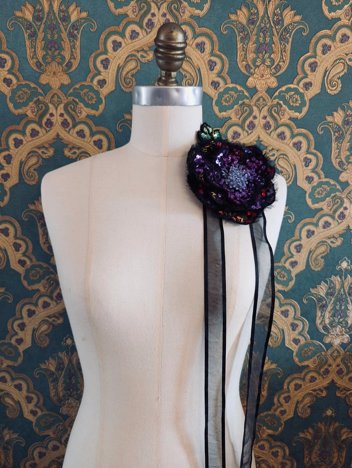 Broochella Luminosa hand beaded sequin choker and brooch in pink and black. Pictured on a mannequin. The background is green and gold damask wallpaper.
