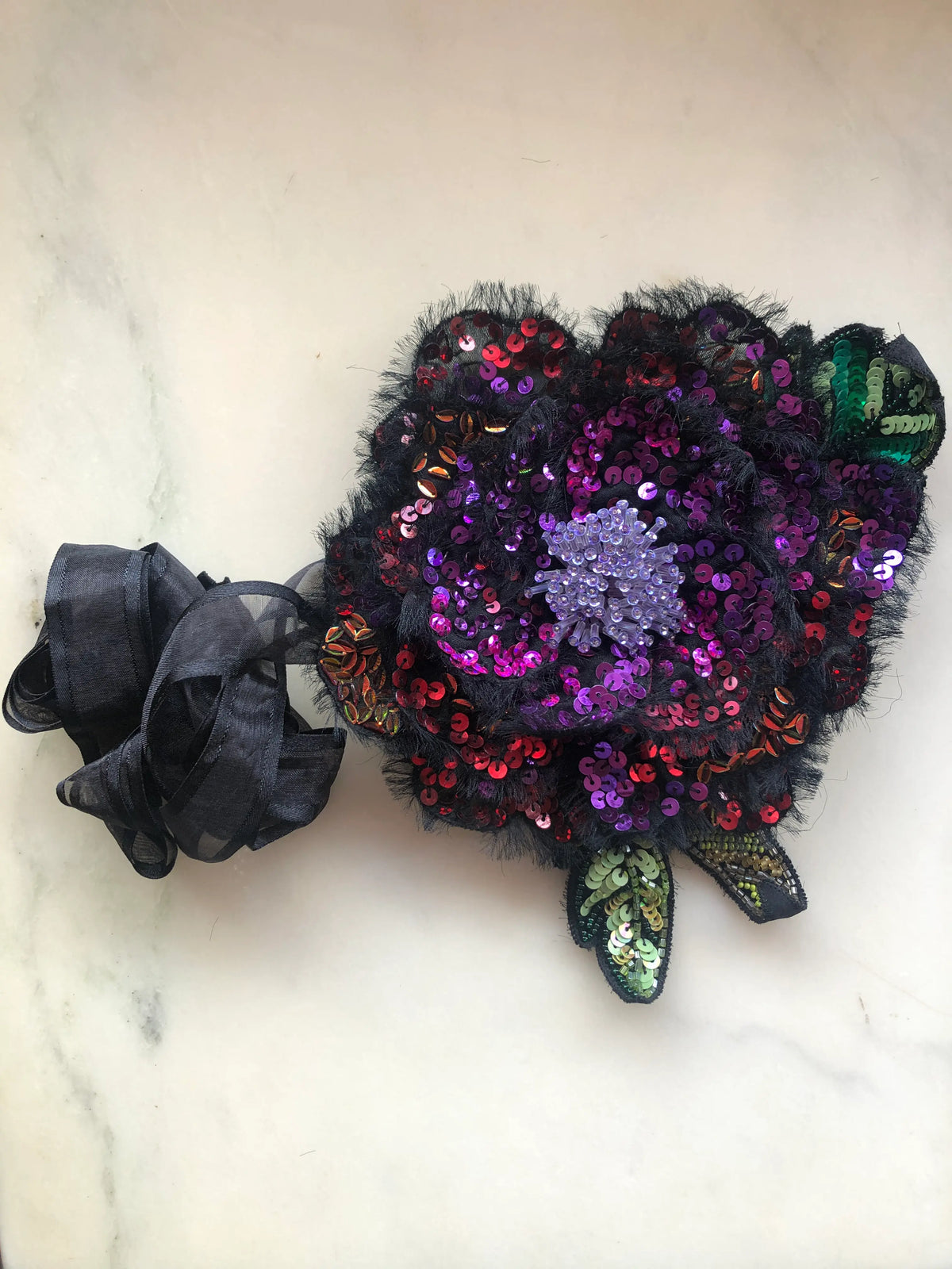 Broochella Luminosa large flower choker and brooch, hand embellished with pink, purple and red sequins, iridescent beads and a beaded centre, with black organza ribbon, photographed on white marble.
