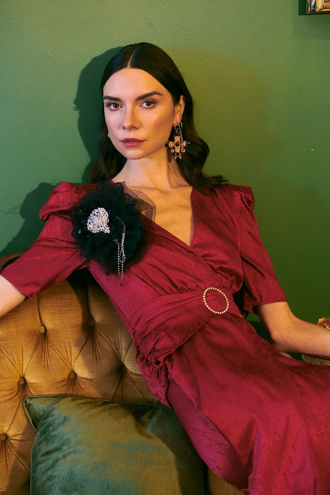 Broochella Madonna black lace embellished handmade designer brooch. Pictured on a model with dark hair in a red dress. The background is green