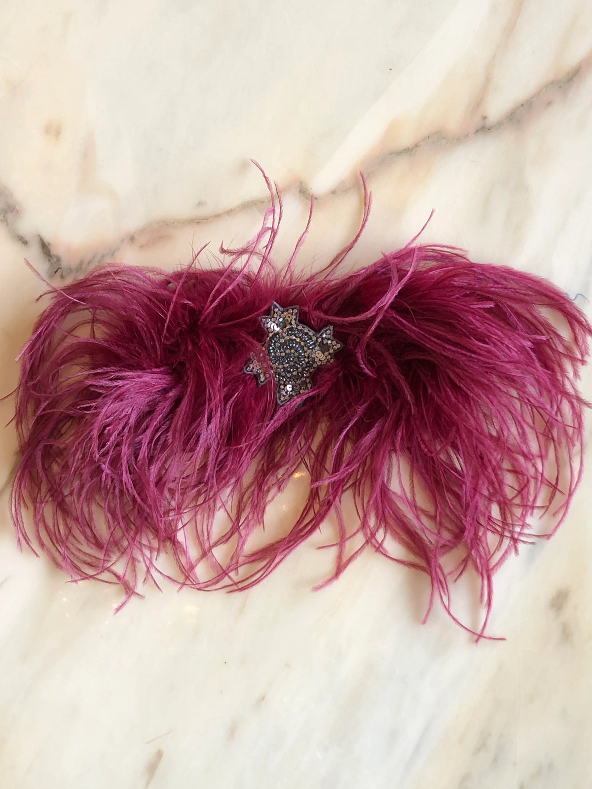 Broochella handmade Magenta Feather Bow Brooch featuring dramatic ostrich feathers and an ornate jewelled centre, an oversized designer statement brooch photographed on a white marble background.