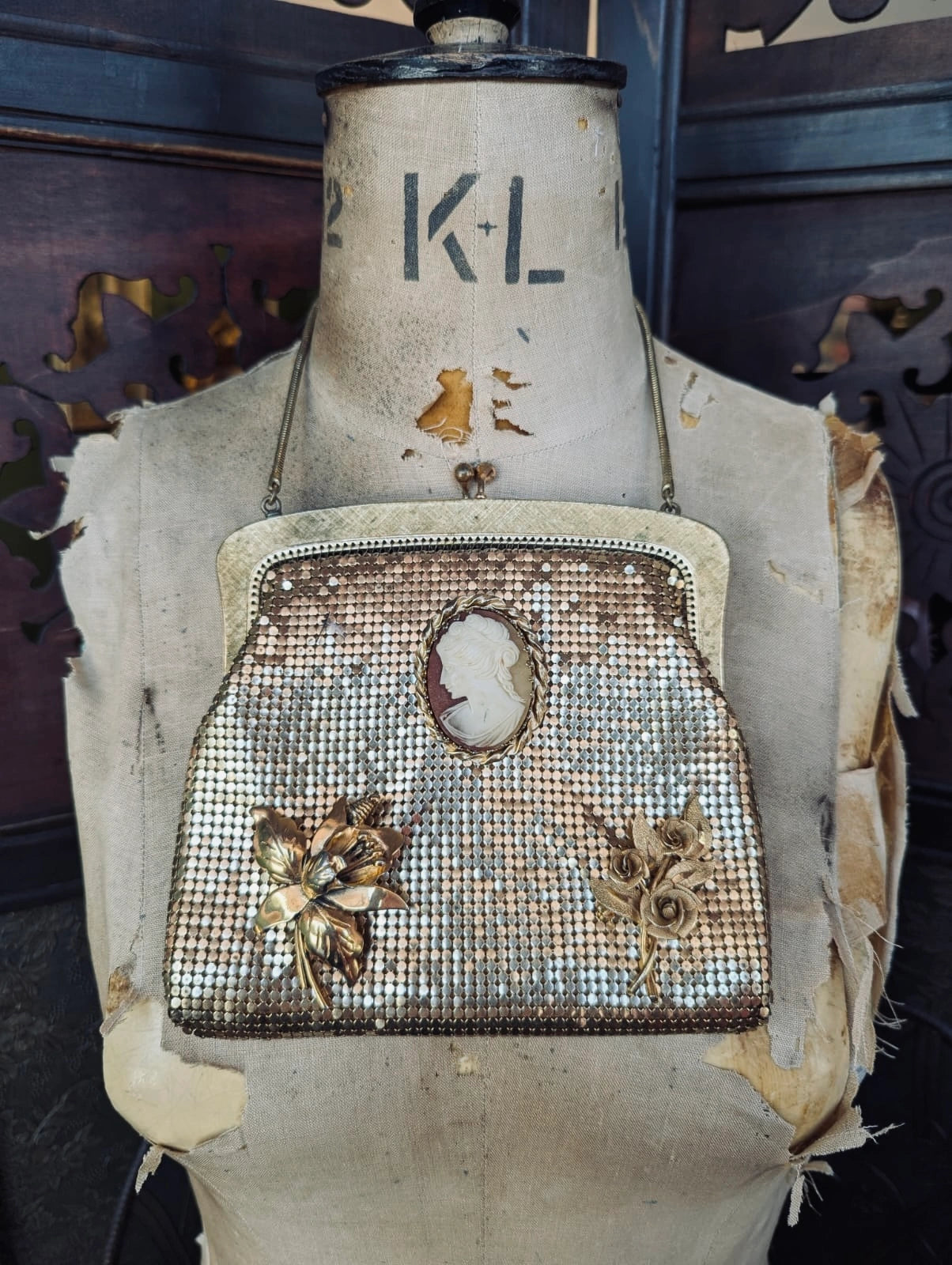 Broochella  la dame d'or oroton gold, glomesh vintage bag with vintage brooch embellishments. Pictured hanging over a vintage mannequin. The background is a decorative, wooden screen. 