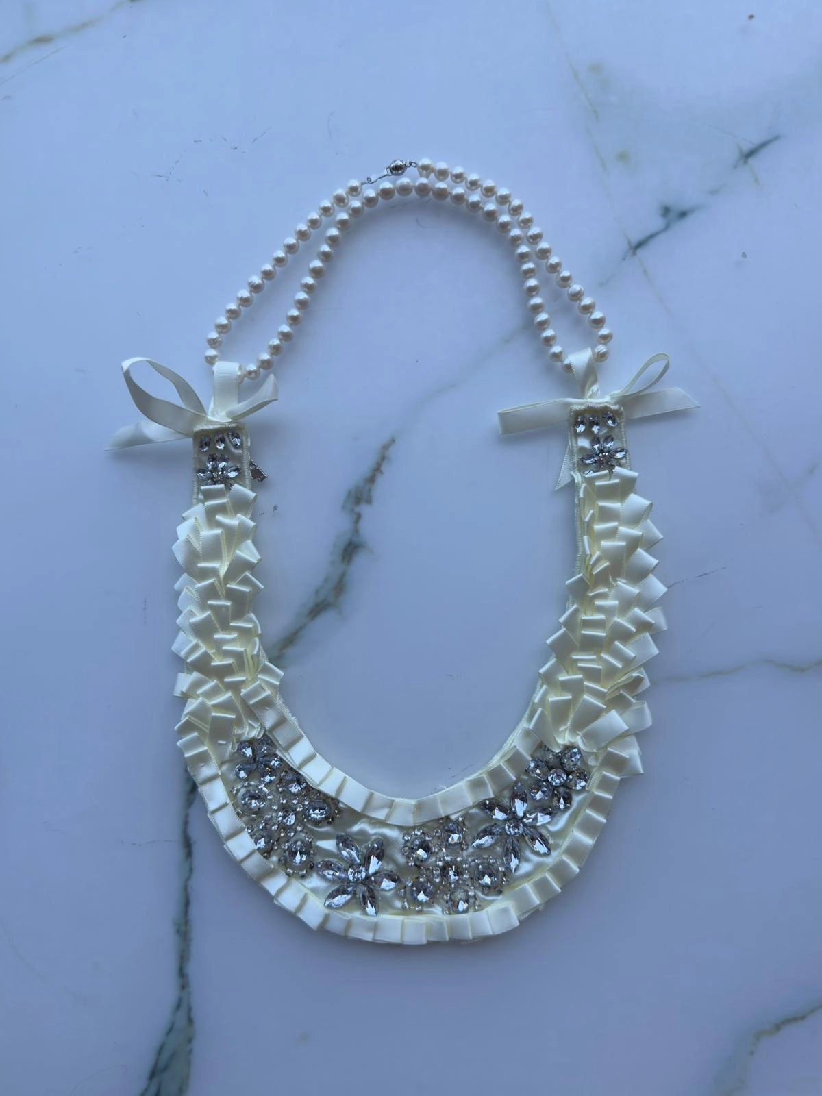 Broochella Maison Broche la Lumiere blanche handamde, ivory satin, crystal, embellished bib/necklace. Pictured with the Broochella freshwater pearl necklace.  Pictured on a white marble background. 