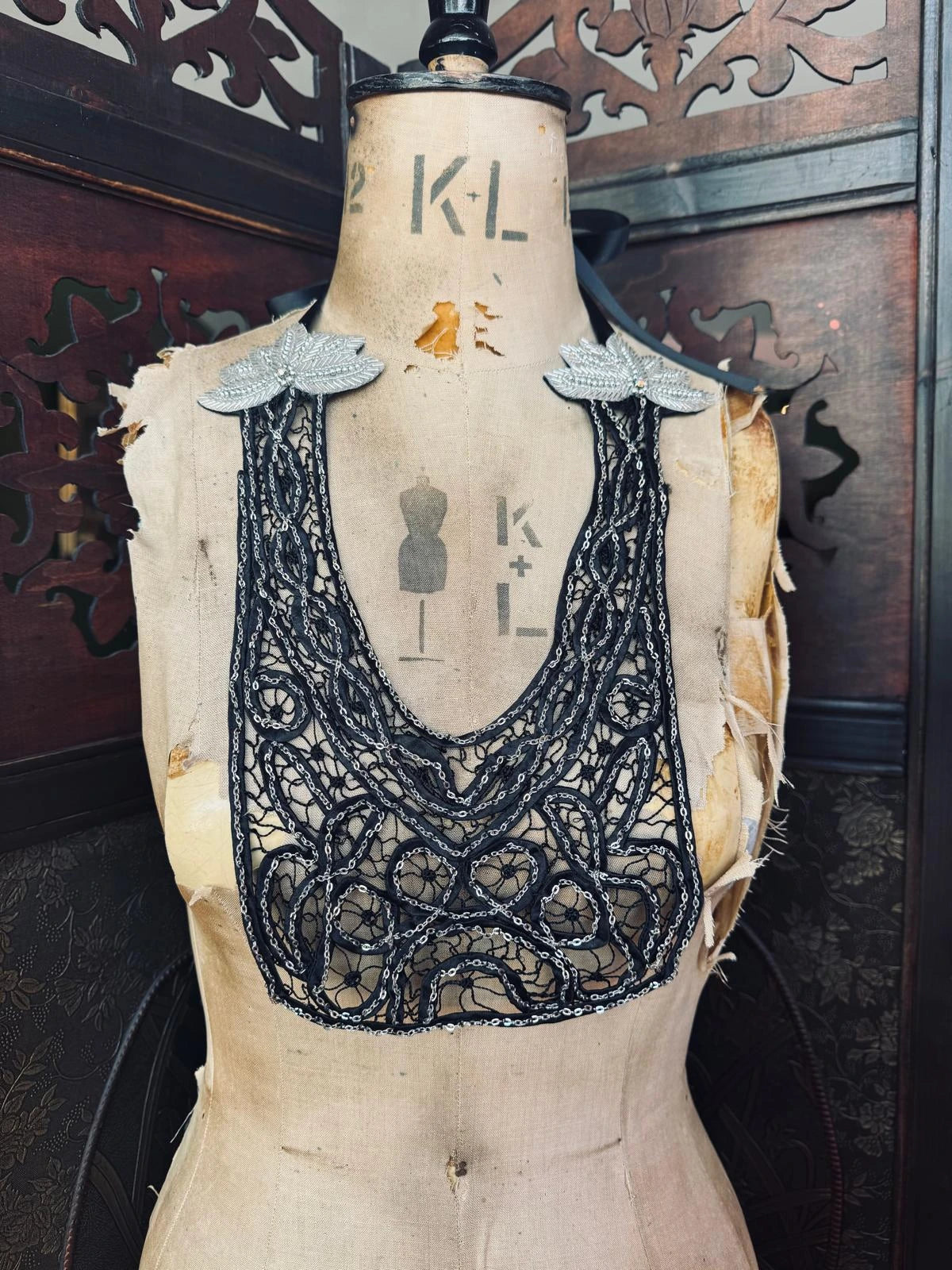 Broochella Maison Broche Le Coeur black, handmade lace and chain bib/necklace. Pictured on a vintage mannequin. The background is a decorative, wooden screen