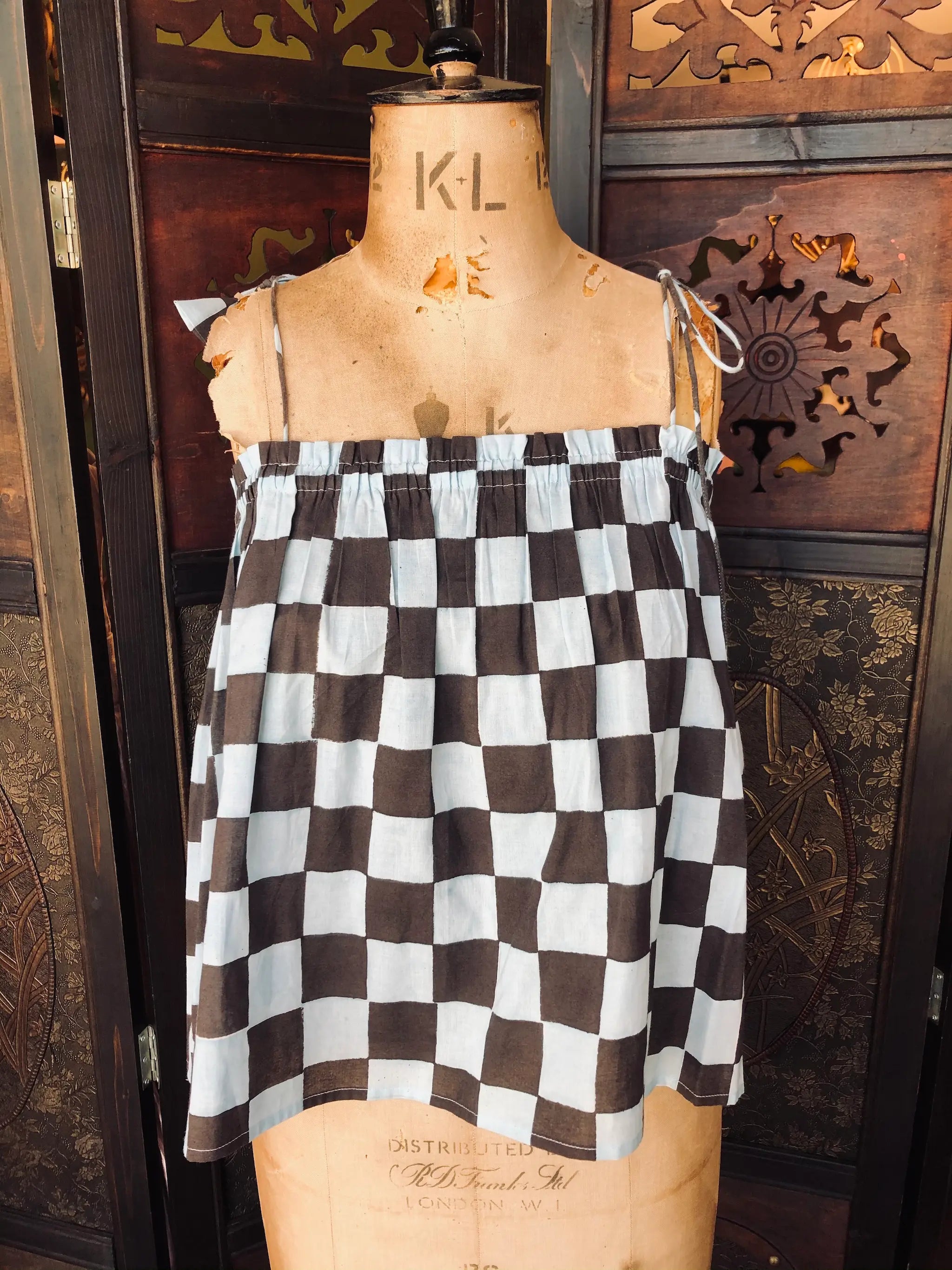 Broochella Malabar Collective blue and black checkered cotton top. It is presented on a vintage mannequin against a decorative wooden background