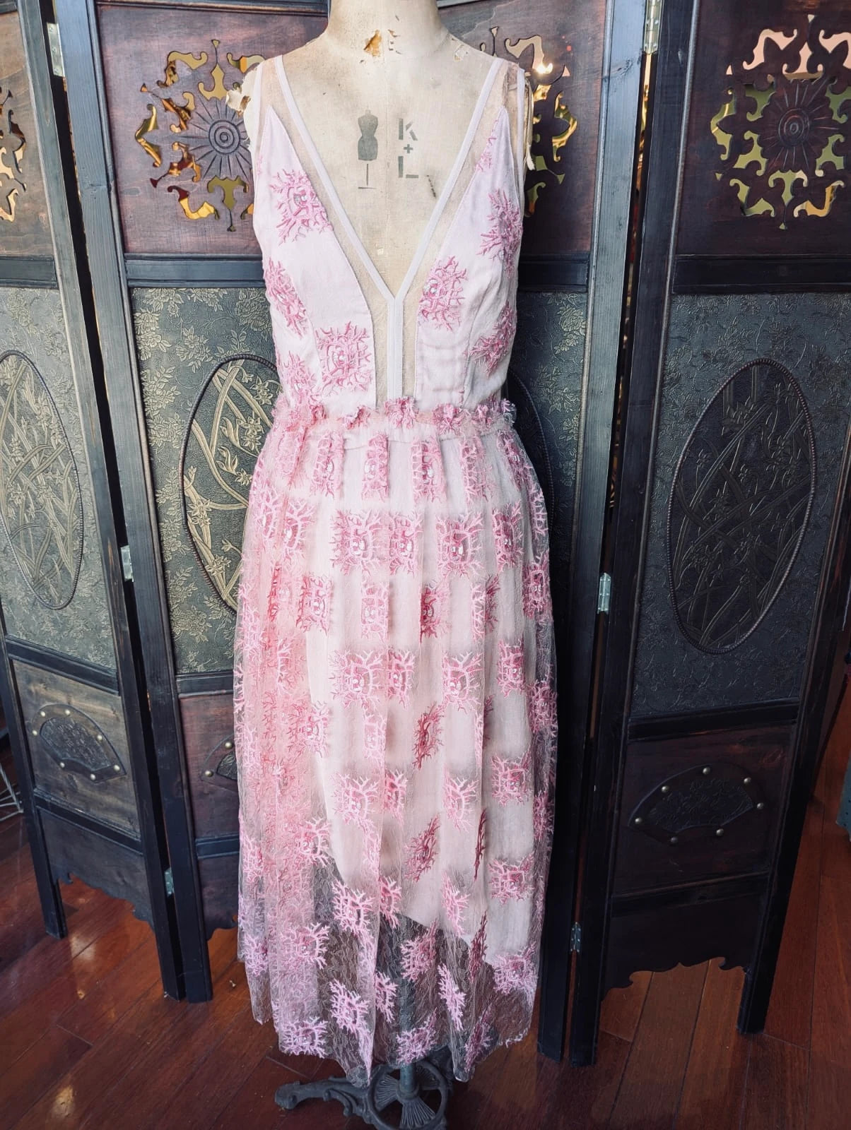 Broochella Manning Carte sleeveless pink and white floral lace dress displayed on a mannequin torso in front of a dark wooden folding screen. 