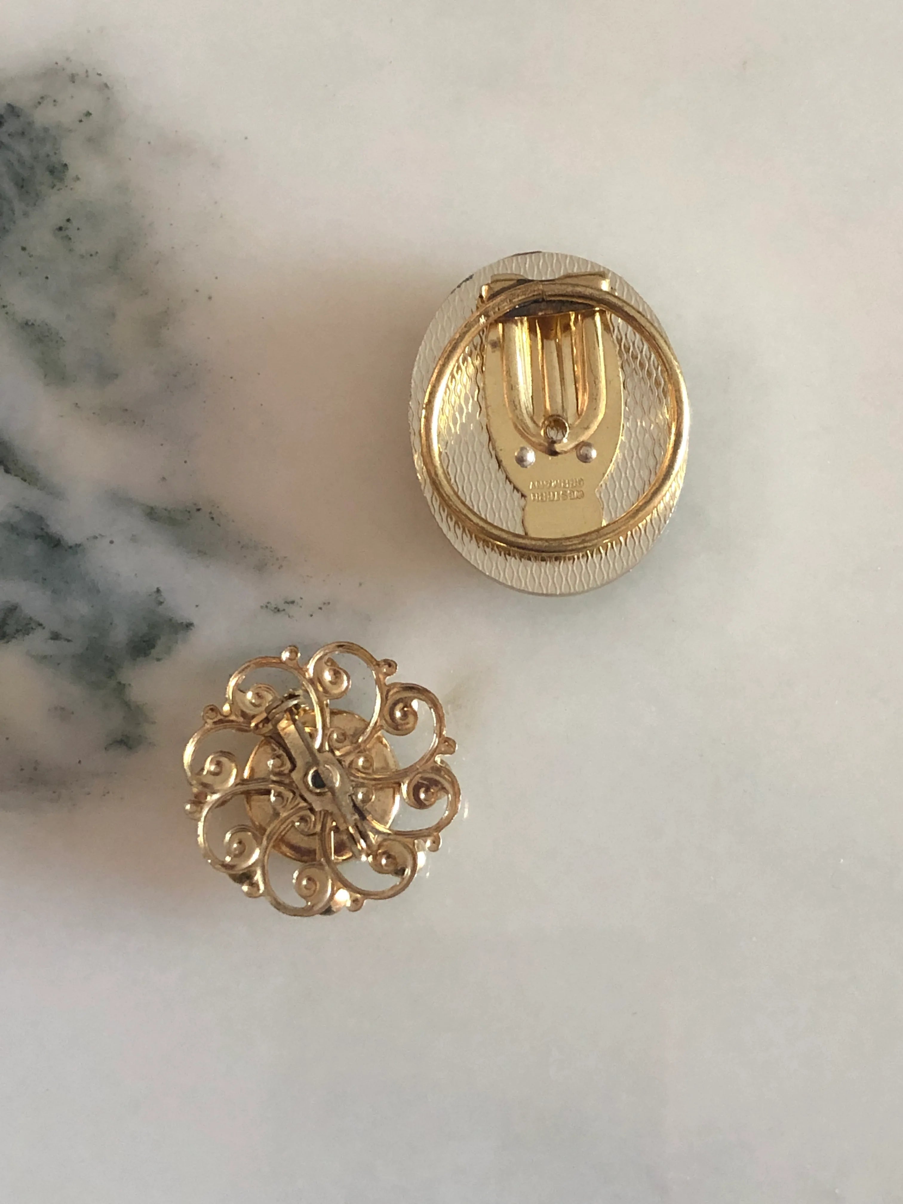 Broochella Cavaliere vintage cameo tie clip and brooch set. They are black and white with decorative metal frames. They are displayed on a white marble table