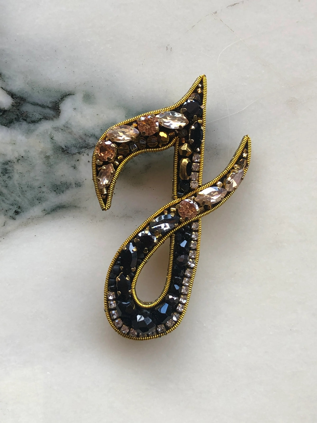 Broochella Men's Initial I Brooch embellished with black beads, clear crystals and champagne stones with gold detailing, photographed on a white marble background with soft grey veining.