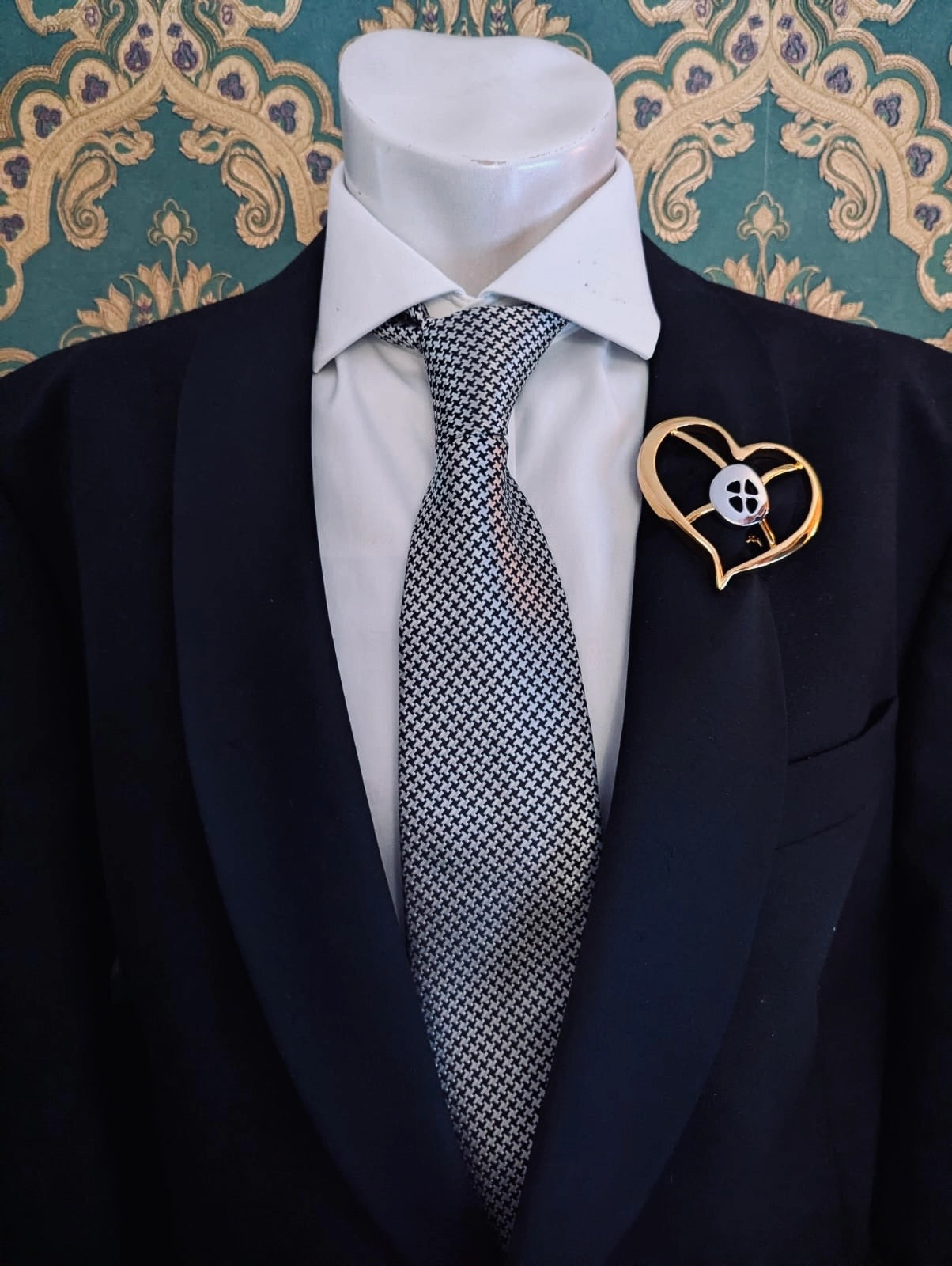 Broochella men's brooches with meaning hope gold metal and silver brooch. Pinned to a men's mannequin wearing a black suit and houndstooth tie. The background is green and gold damask wallpaper.
