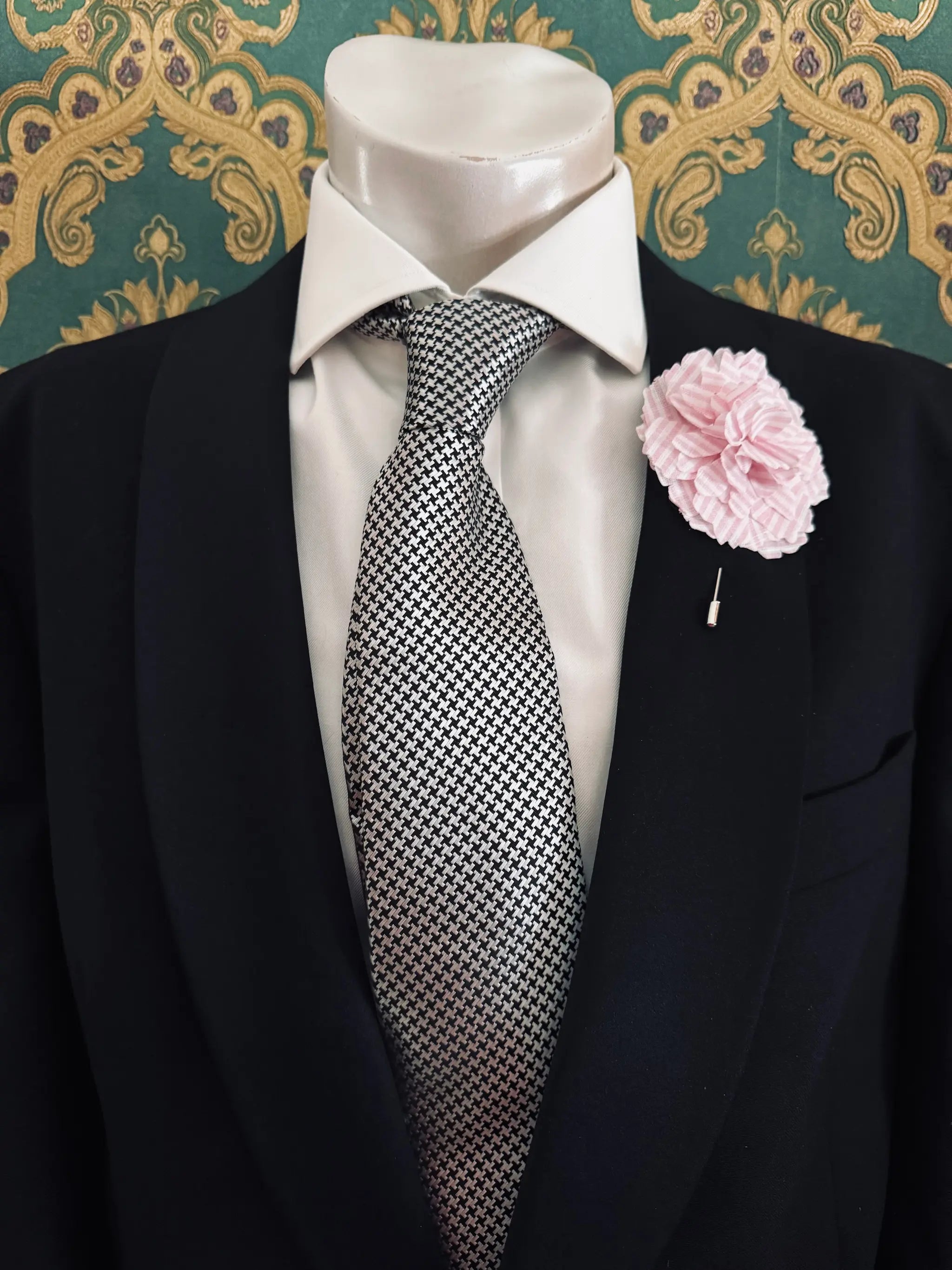 Broochella men's handmade linen carnation brooch in pink and white. Pinned to a men's mannequin wearing a black suit and a tie. The background is green and gold damask wallpaper.
