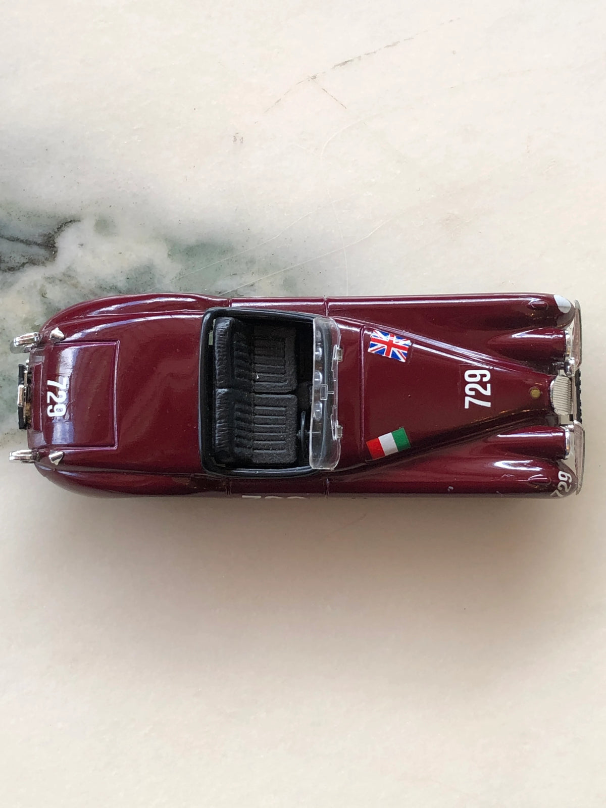 Broochella Men's Barolo No.729 Vintage Racing Car Brooch photographed from above, showcasing its glossy burgundy body, number 729 markings, British and Italian flag decals, clear windscreen and black interior.