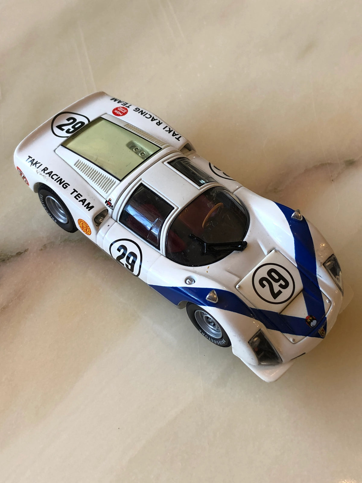 Broochella Men's Bianco Takumi No.29 Vintage Racing Car Brooch, featuring a white endurance racing car with bold blue stripes, number 29 decals, Taki Racing Team branding, silver wheels and a detailed cockpit