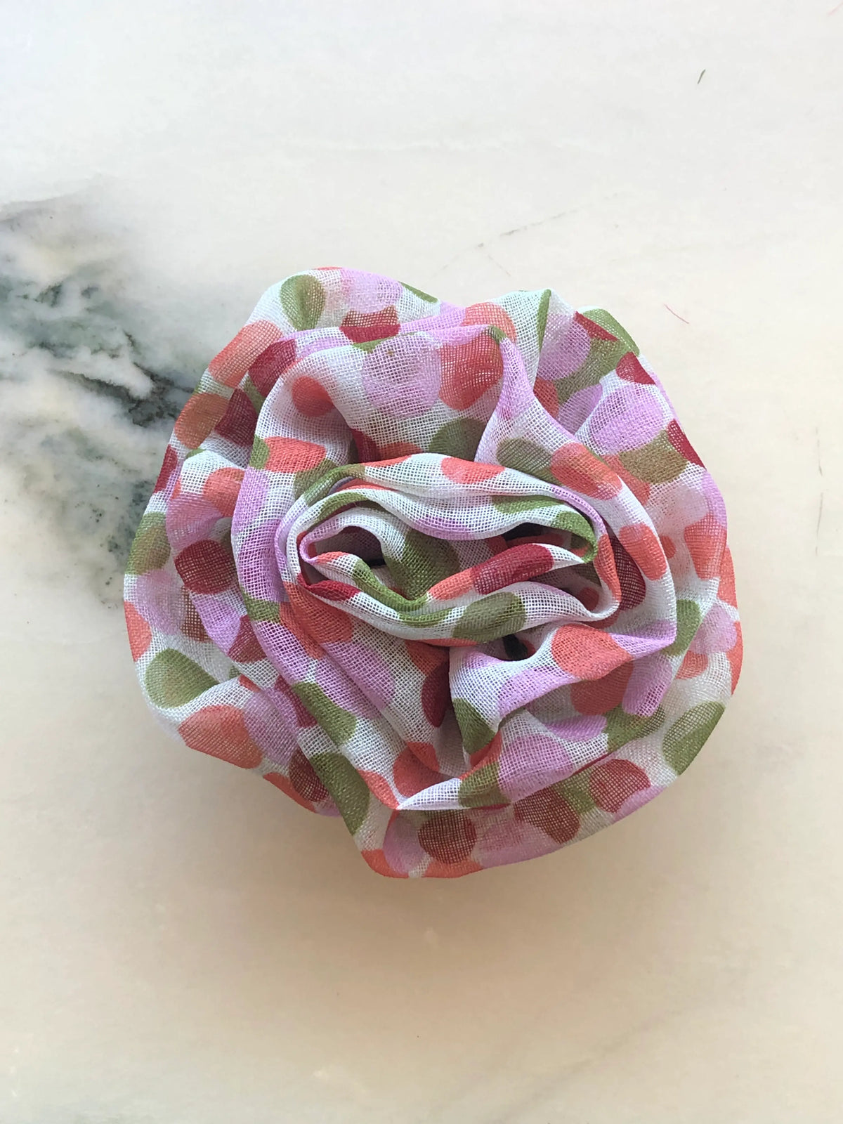 Broochella Men’s Brassica Flower Brooch in pink, a handmade designer fabric flower with sculptural layered petals and pink, coral and green print, photographed on white marble.