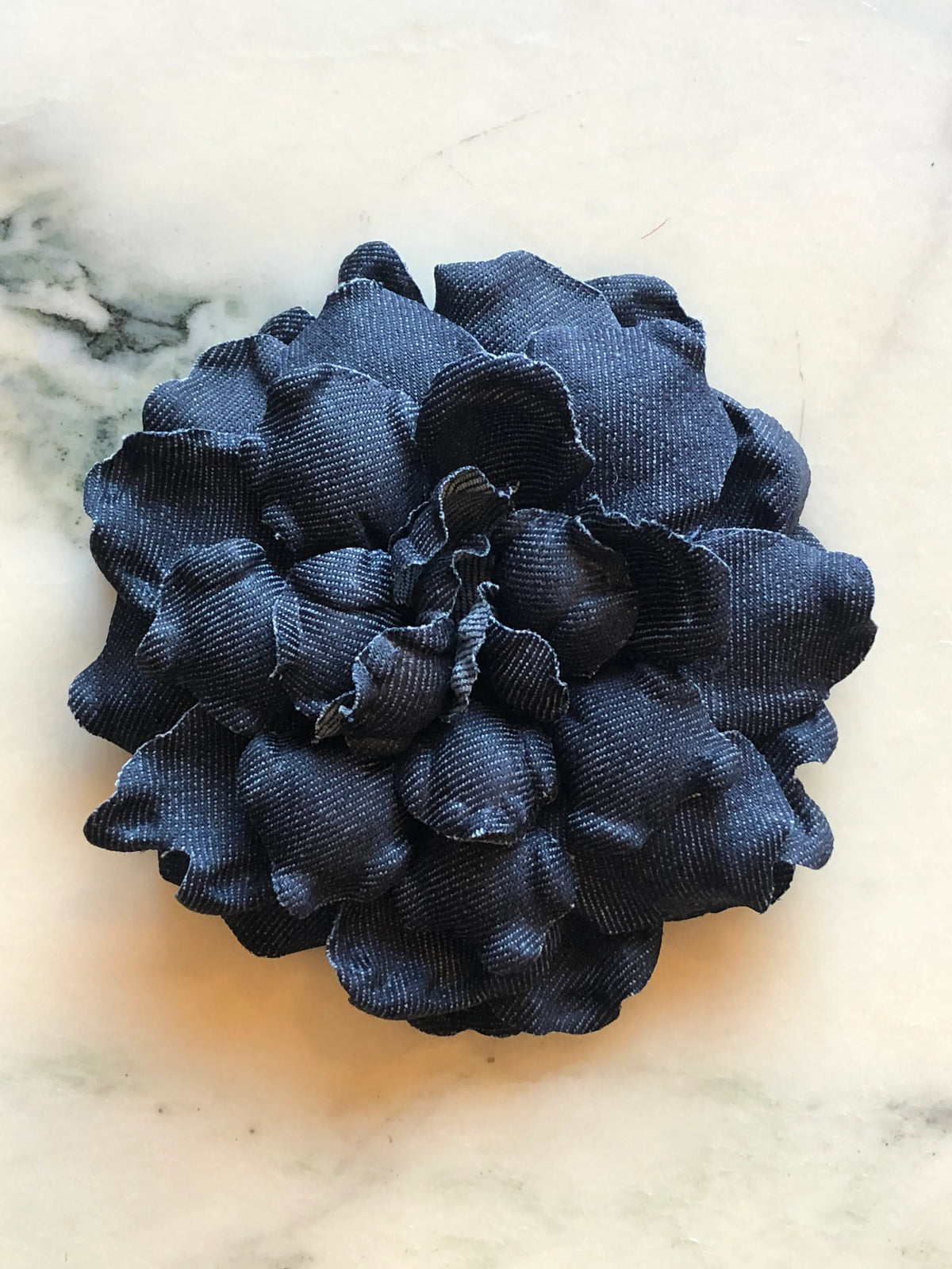Broochella Men’s Denim Flower Brooch in navy, a handmade designer statement flower with sculptural layered denim petals, photographed on a white marble background.
