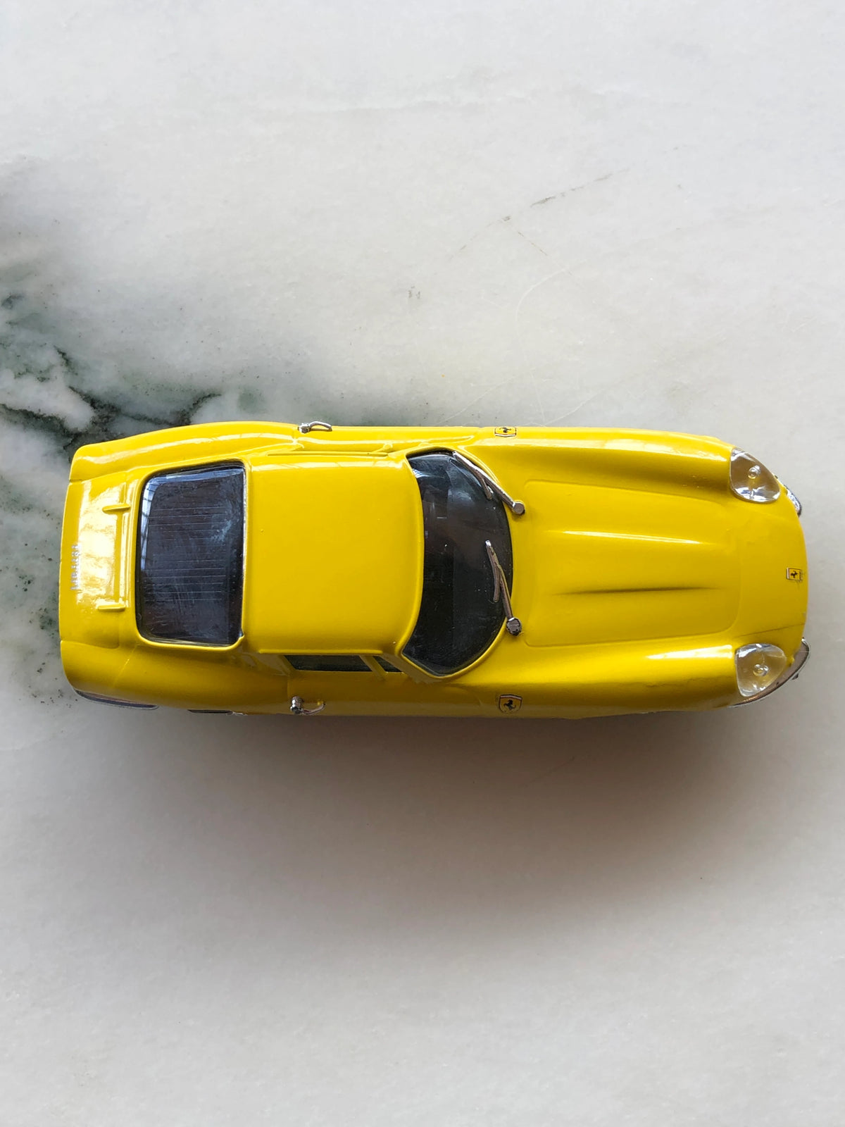 Broochella Men's Giallo Fiorano No.275 Vintage Ferrari Racing Brooch viewed from above, showcasing its glossy yellow bodywork, sculpted bonnet, black windscreen, streamlined roof and rear window detailing.