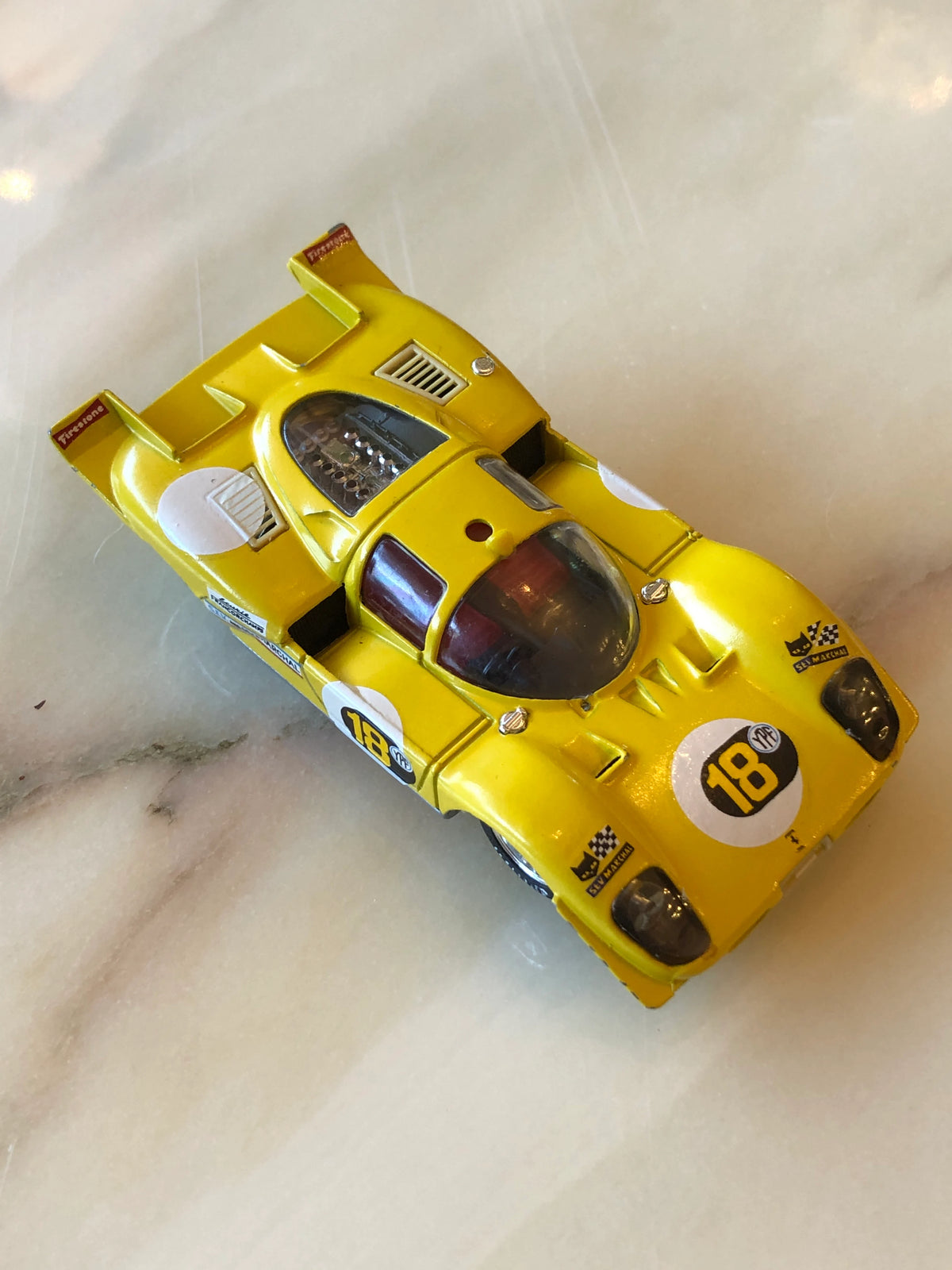 Broochella Men's Giallo Modena No.18 Vintage Racing Car Brooch in bright yellow, featuring black number 18 decals, aerodynamic bodywork, clear cockpit canopy, rear racing spoiler and Firestone detailing.