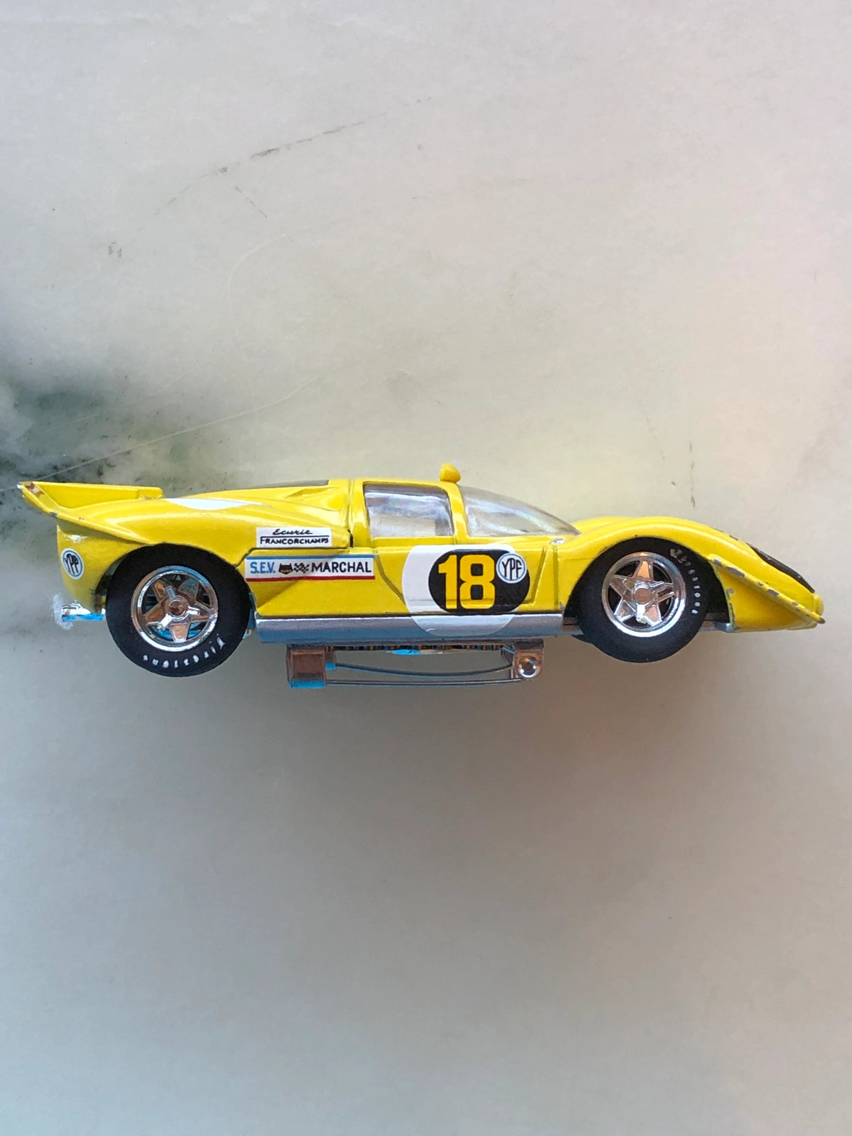 Broochella Men's Giallo Modena No.18 Vintage Racing Car Brooch in side profile, featuring a yellow aerodynamic body, black number 18, chrome wheels, racing sponsor decals, rear spoiler and metal brooch pin fastening.