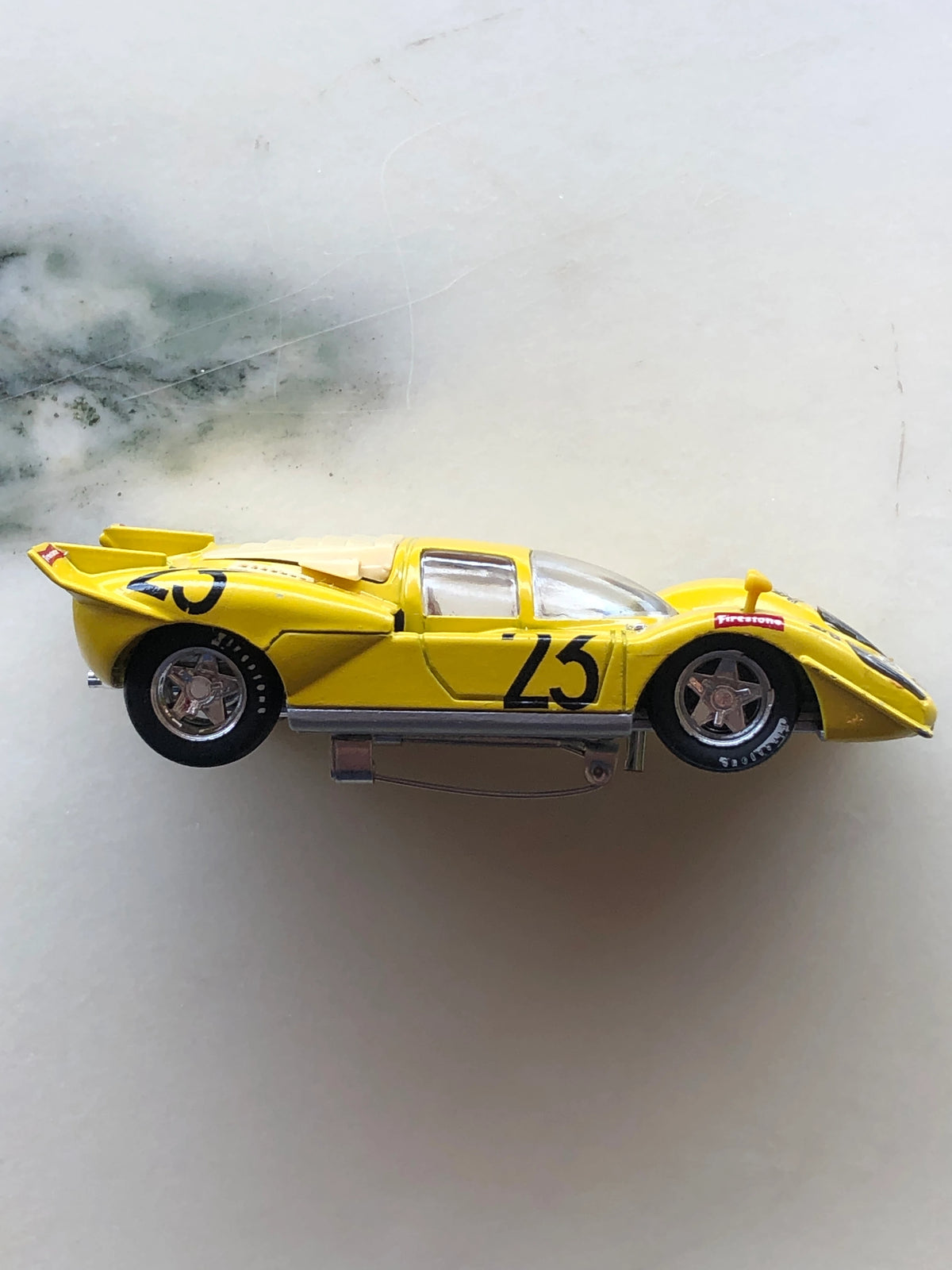 Broochella Men's Giallo Sprint No.23 Vintage Endurance Racing Car Brooch in bright yellow, featuring black number 23 decals, a streamlined body, silver wheels, Firestone detailing and a metal brooch pin fastening underneath.