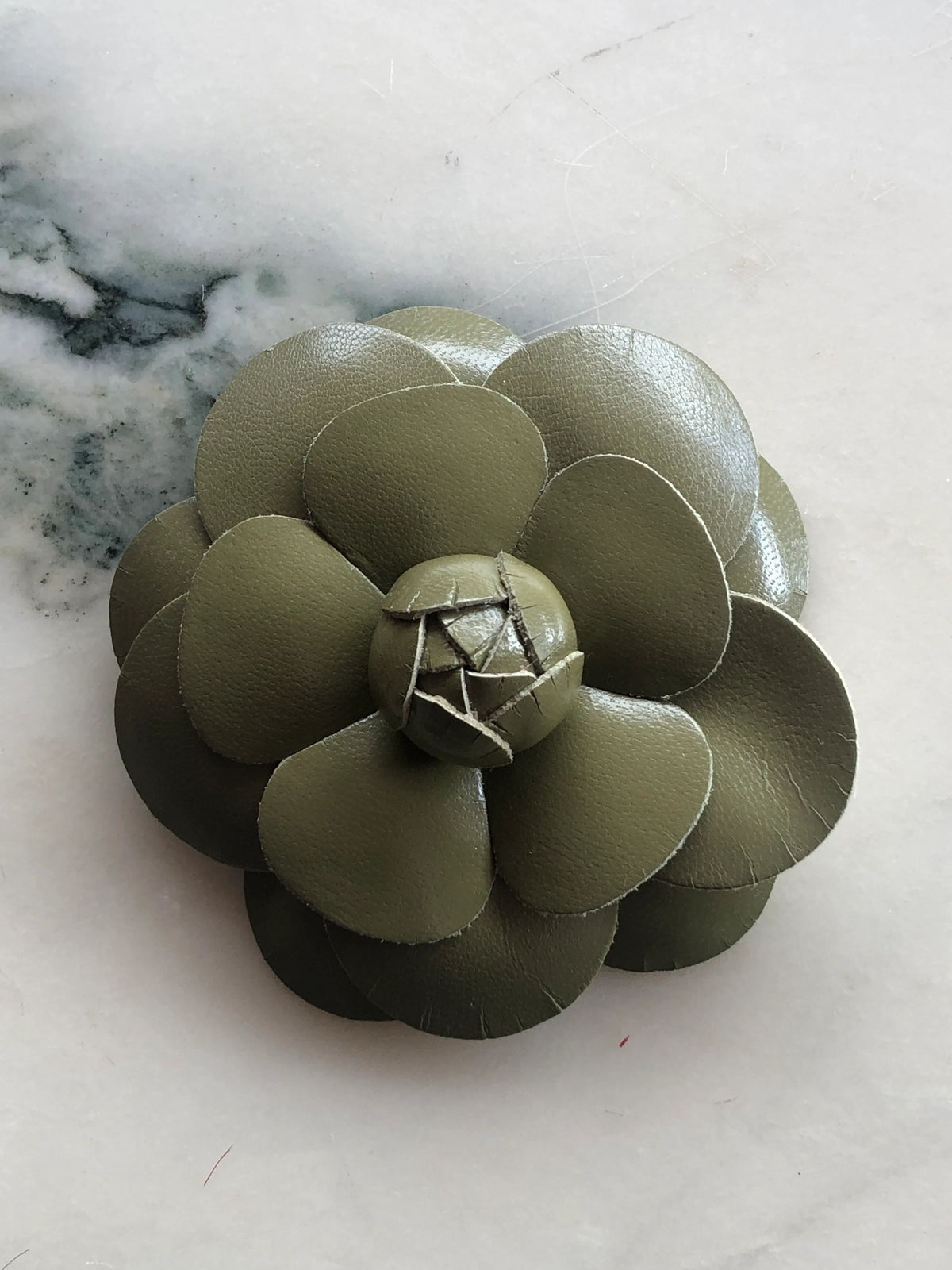 Broochella Men’s Leather Camelia Brooch in avocado green, a handmade designer leather flower brooch with layered sculptural petals and bud centre, photographed on white marble.