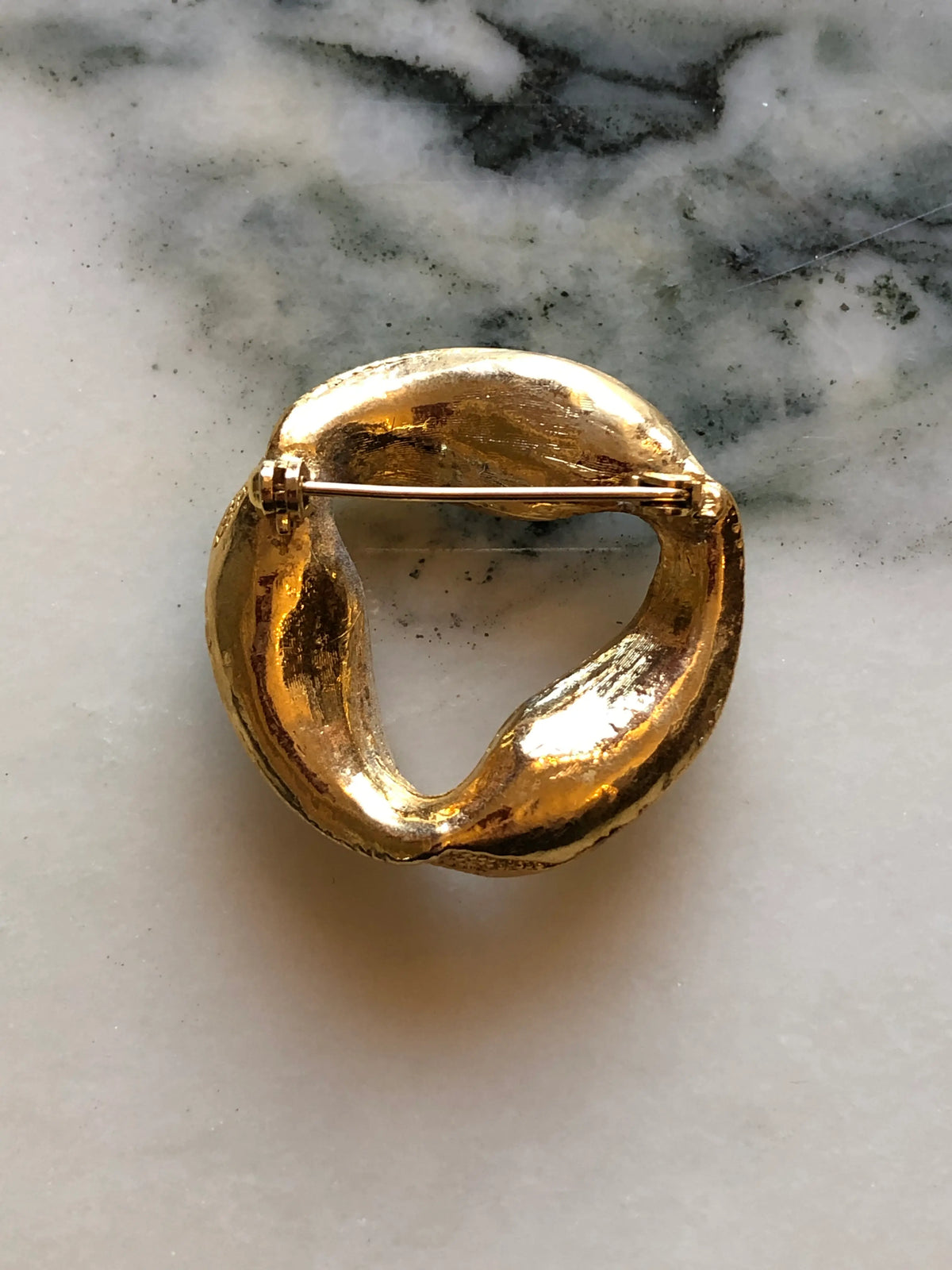 Broochella Men's Ottavia Vintage Black & Crystal Swirl Brooch featuring black and clear crystals set into a sculptural gold-tone circular design on a cream and grey marble background.