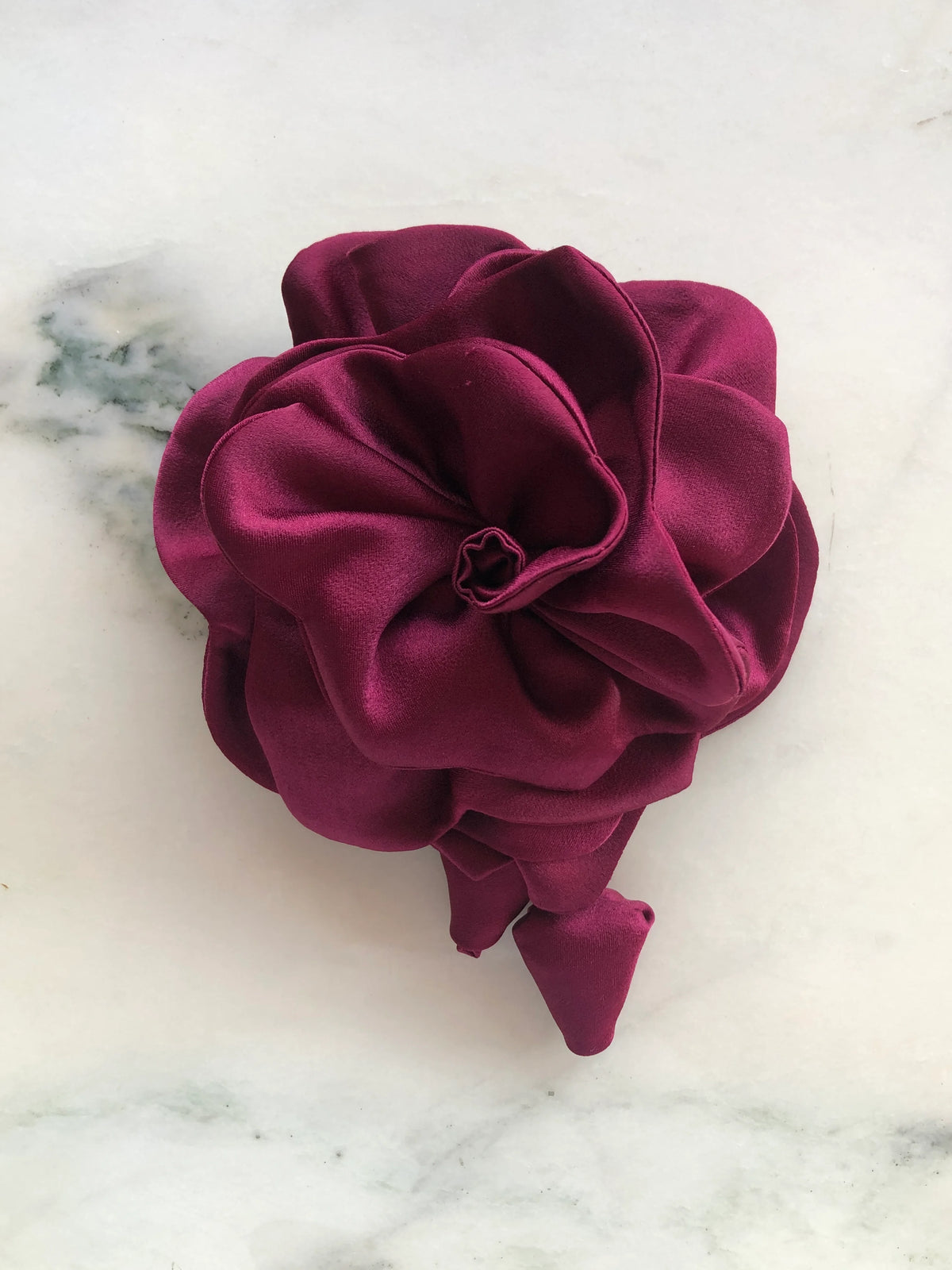 Broochella handmade designer satin Rosetta flower brooch in burgundy with sculptural layered petals and trailing flower buds, photographed on white marble.