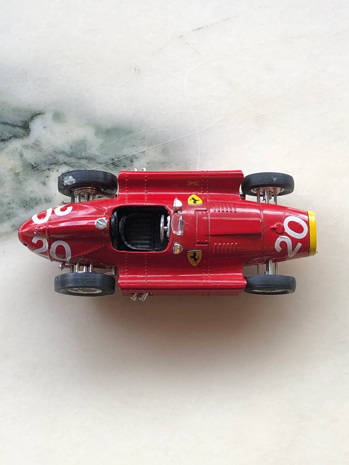 Broochella Men's Rosso Classico No.20 Vintage Ferrari Racing Car Brooch viewed from above, showcasing its glossy red body, white number 20 racing decals, black single-seat cockpit, Ferrari shield emblems and yellow front grille.