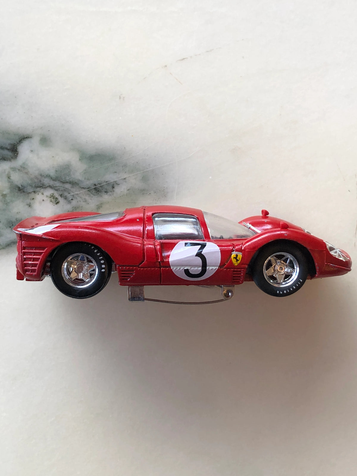 Broochella Men's Rosso Le Mans No.3 Vintage Ferrari Racing Car Brooch in side profile, featuring a red aerodynamic racing body, white number 3 roundel, Ferrari shield emblem, chrome wheels and silver brooch pin fastening underneath.