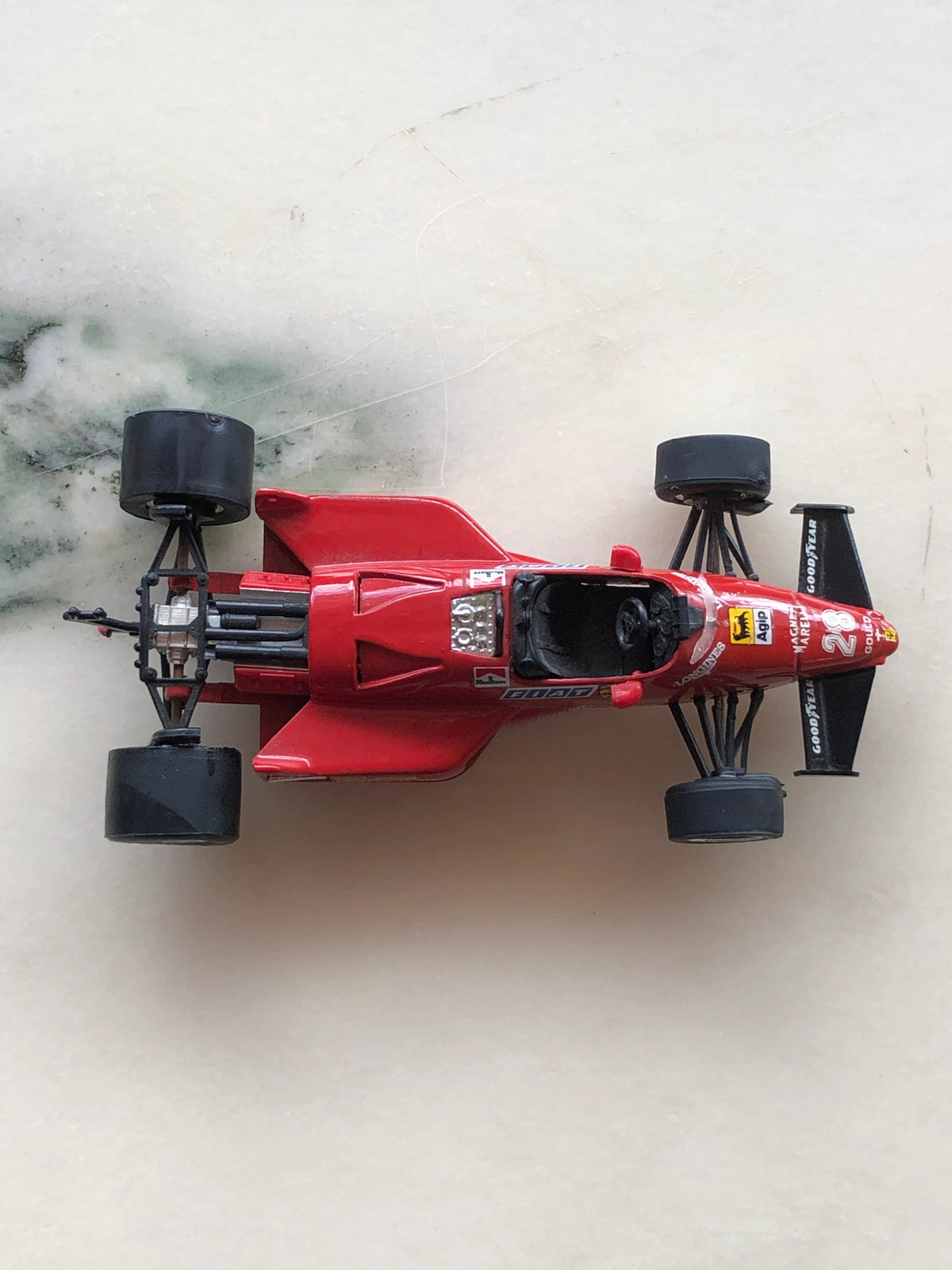 Broochella Men's Rosso Monza No.28 Ferrari Formula One Racing Car Brooch viewed from above, showcasing its red aerodynamic body, black cockpit, exposed rear engine, wide racing tyres, number 28 and vintage sponsor detailing.