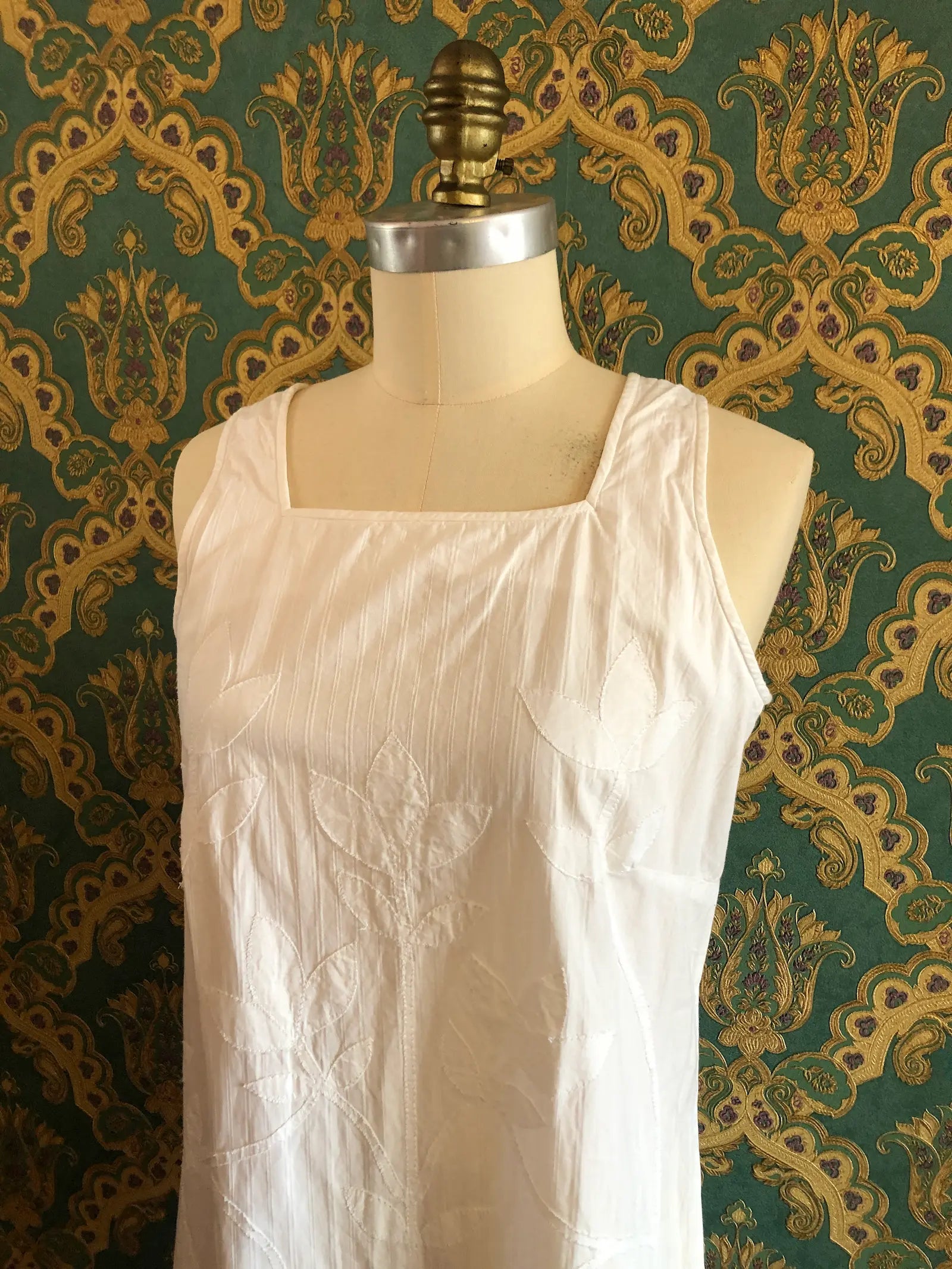 Broochella Mid summer Australia white striped cotton maxi dress with tonal leaf appliqué, size Small. Pictured on a mannequin. The background is green and gold damask wallpaper
