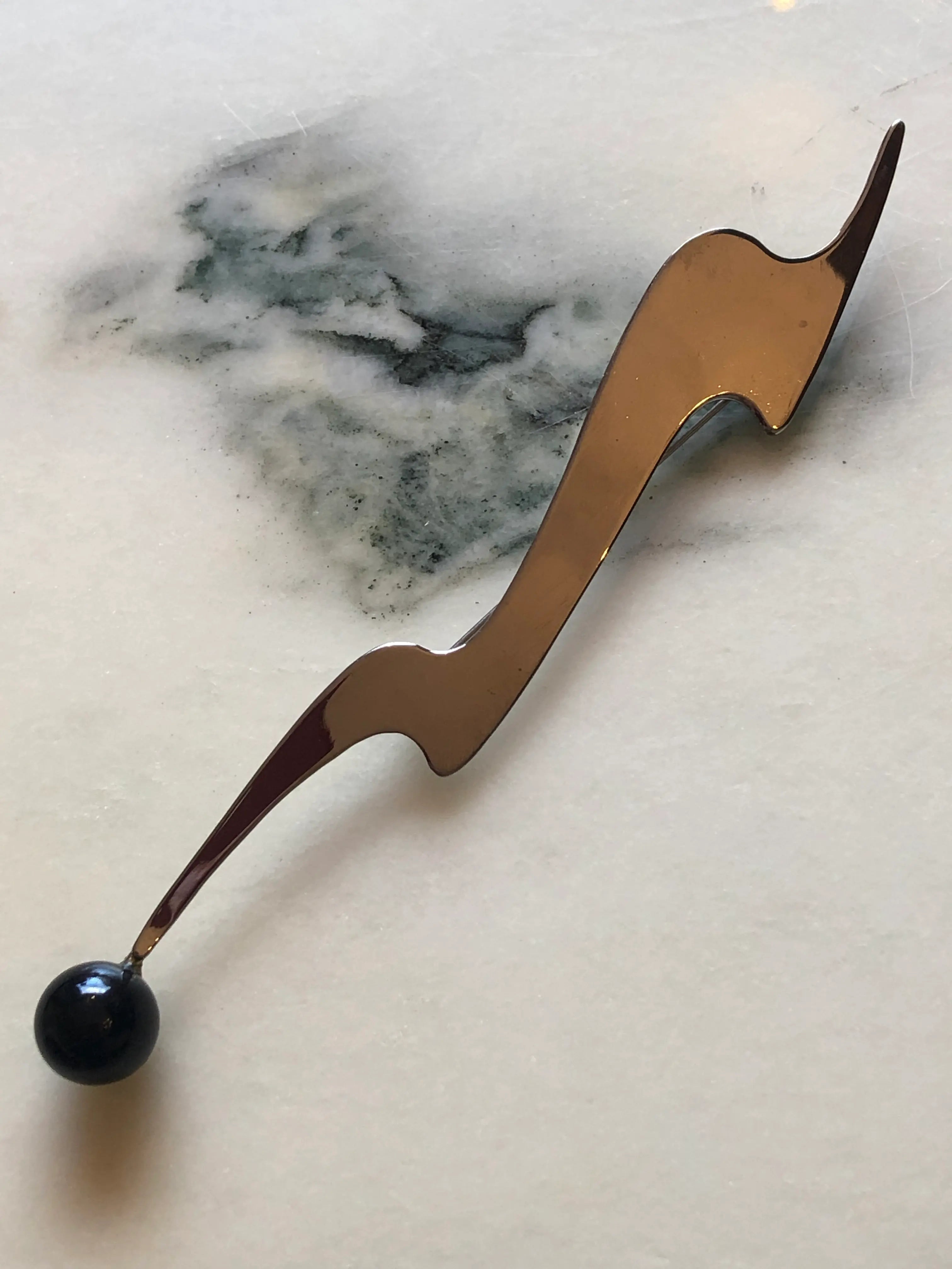 Broochella Midnight Comet vintage modernist brooch in polished silver-tone metal with an elongated abstract shape and glossy black spherical drop, measuring approximately 16.5 × 3 cm. Photographed on white and grey marble.