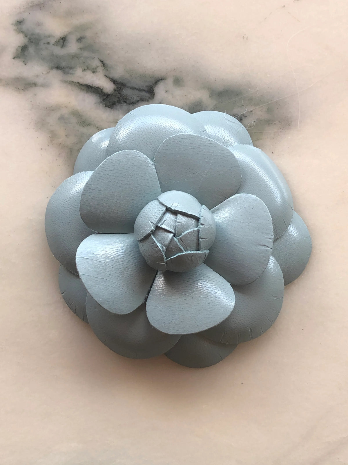 A Broochella Camelia handmade mint green leather flower-shaped accessory brooch,  resting on a white marble surface.