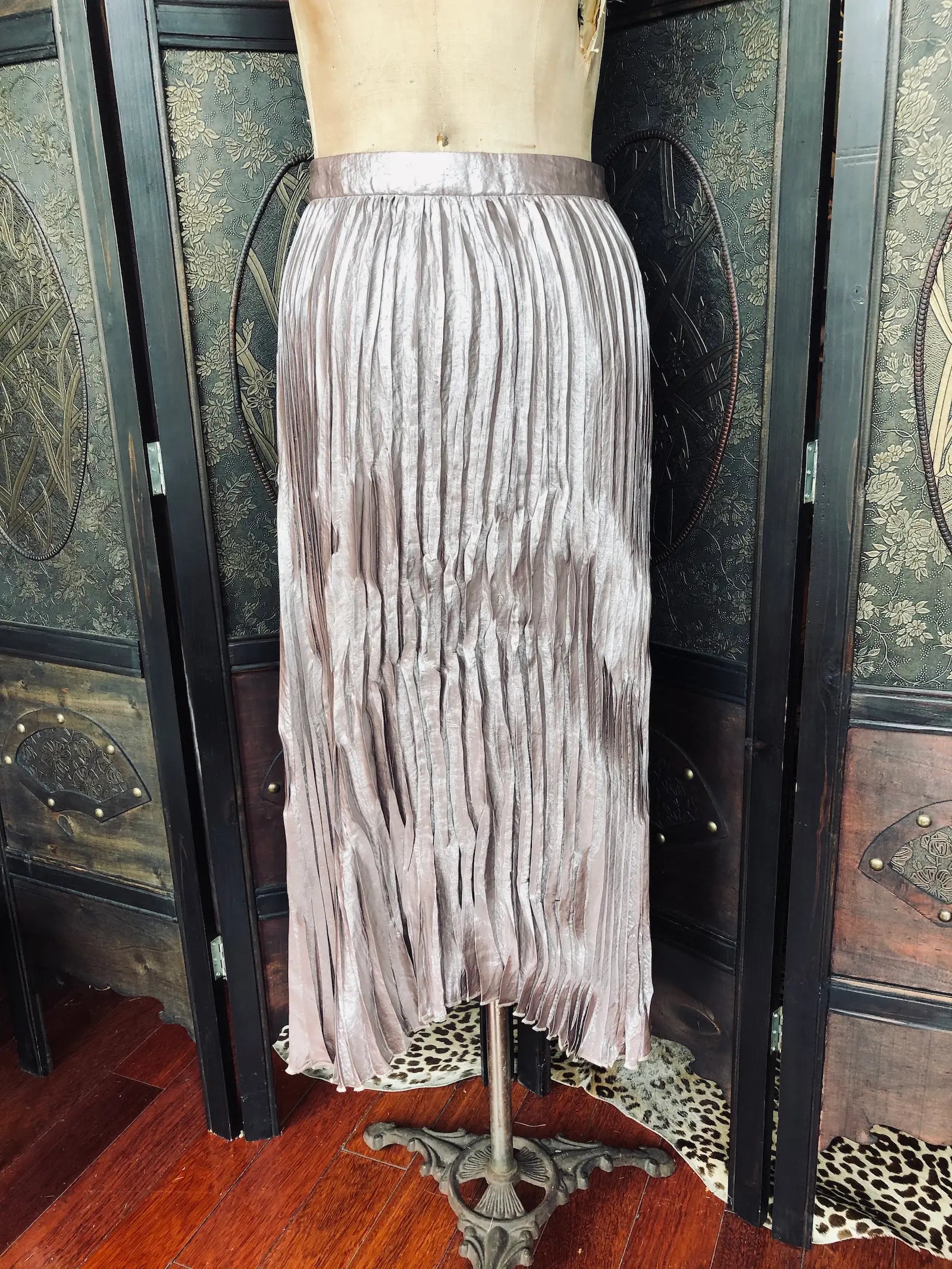 Broochella The Stylist's Closet Momoni pleated midi skirt in a dusty mauve-purple satin-like fabric, displayed on a dress form mannequin in front of a dark folding screen.