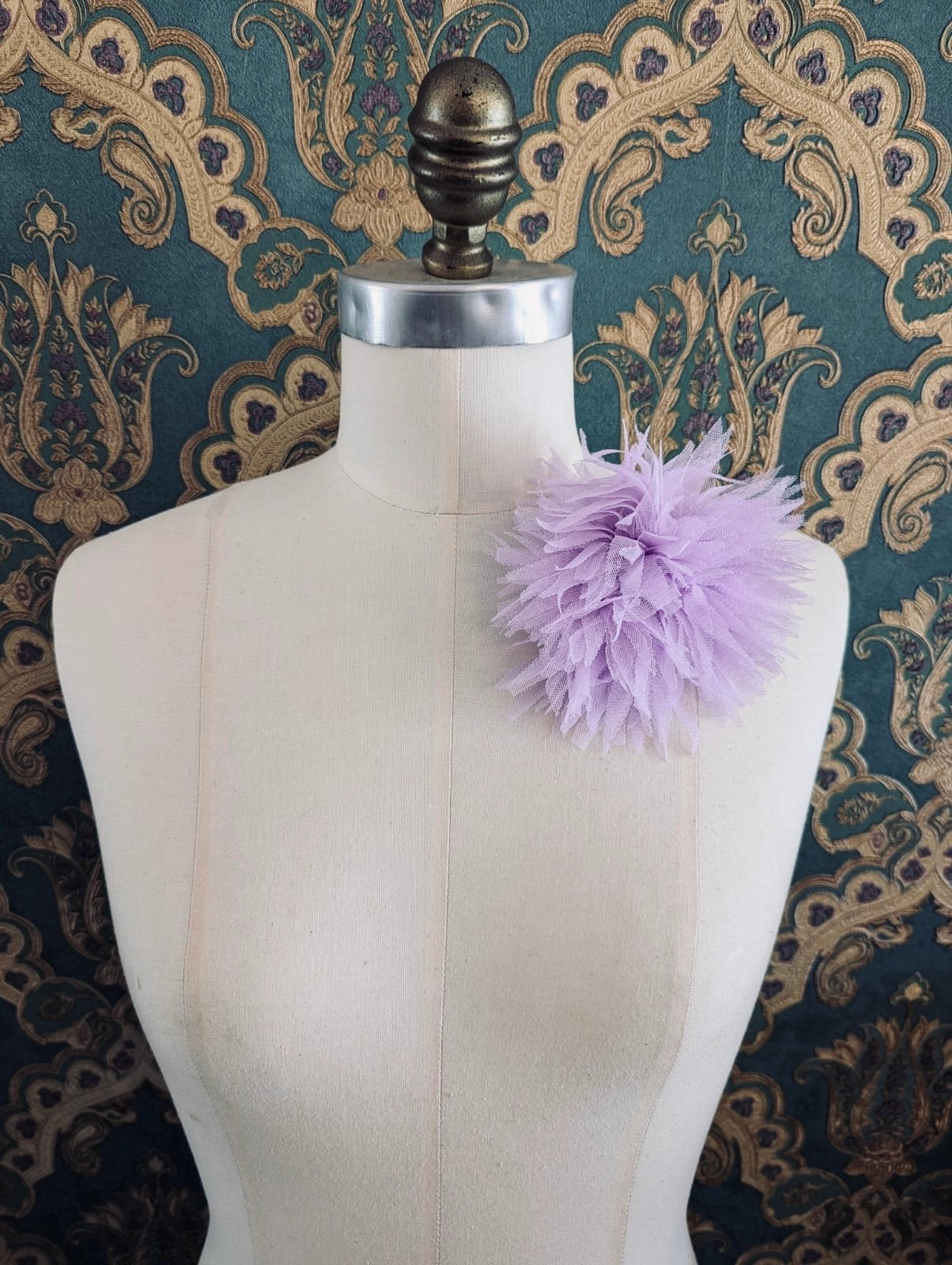 Broochella monello handmade tulle urchin brooch in lilac. The brooch is pinned on a mannequin. The background is green and gold damask wallpaper.