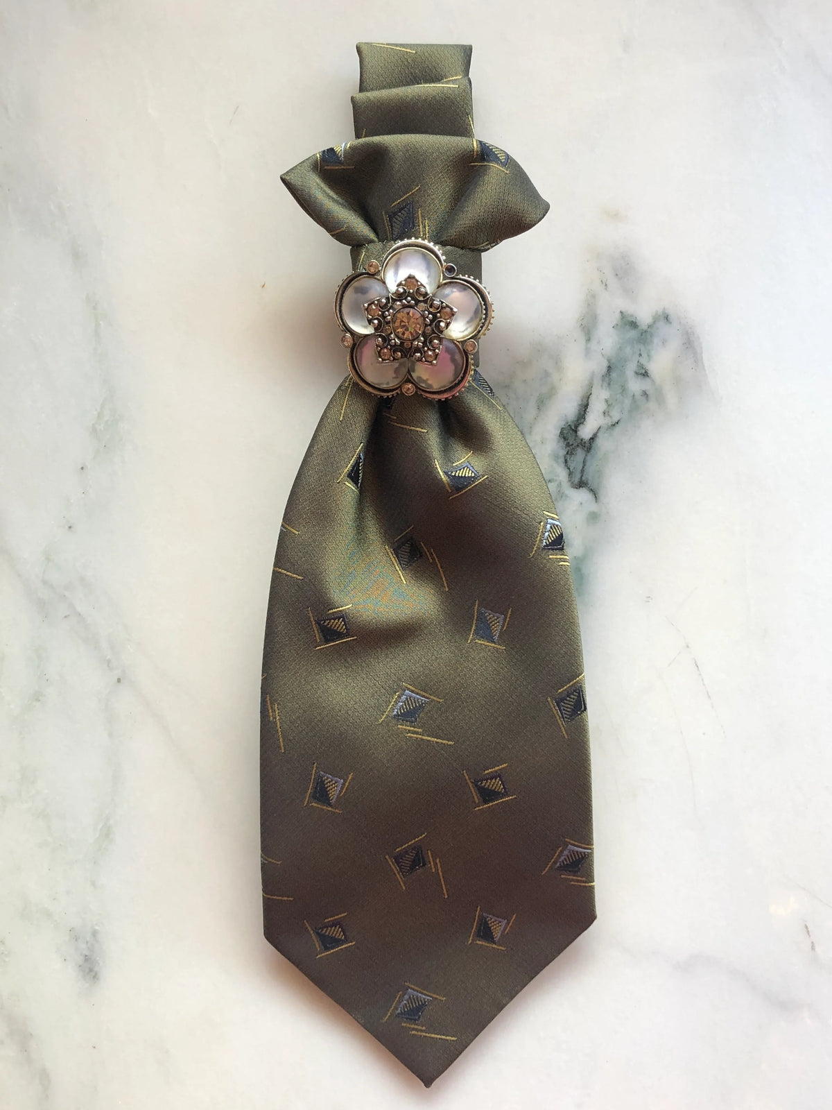 Broochella Montecristo Cravatta Tie Brooch Pin #21, a handmade designer statement brooch crafted from an upcycled vintage olive green silk tie with a subtle geometric pattern, finished with an ornate pearl and crystal flower embellishment, photographed on white marble.