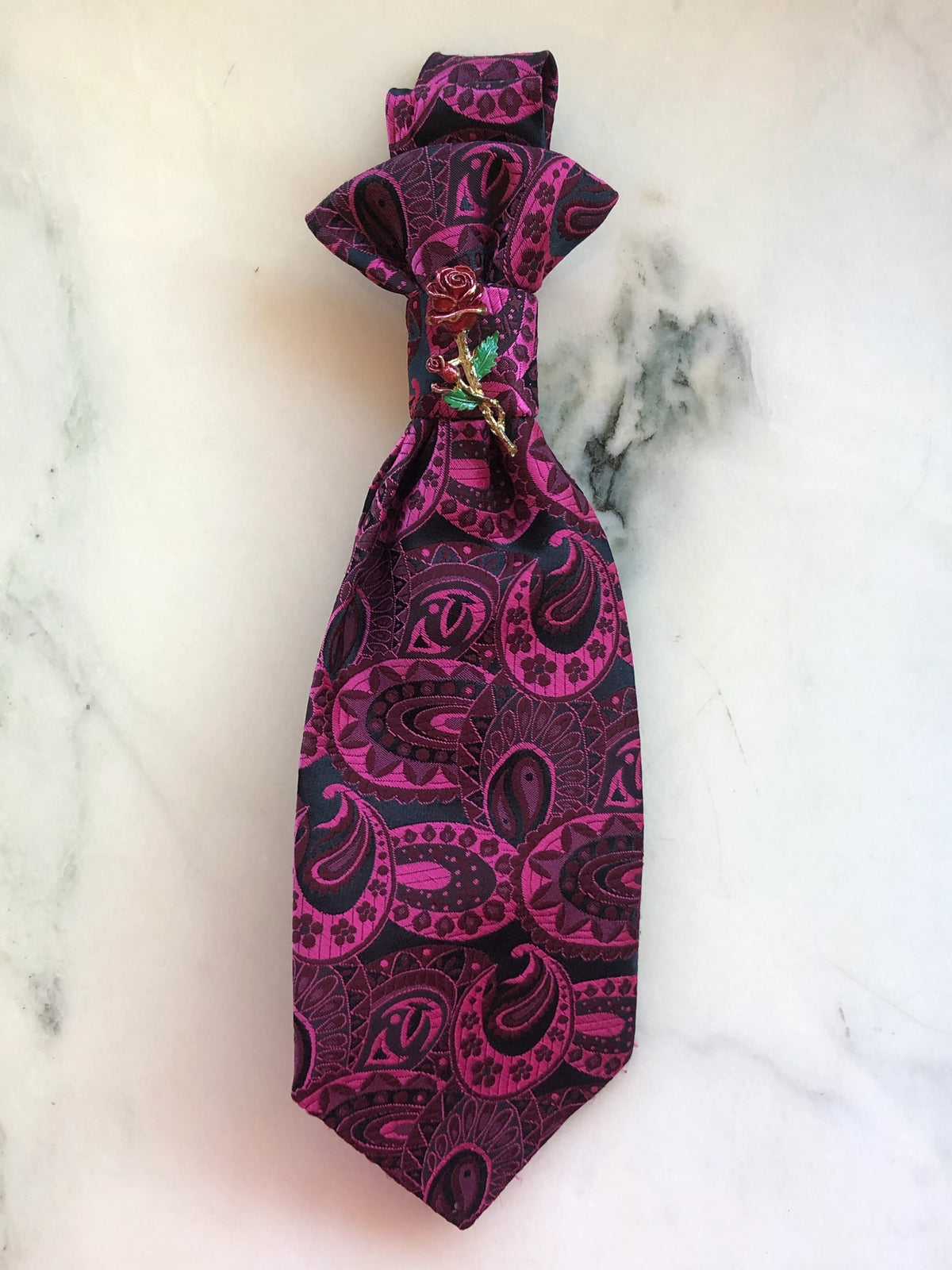 Broochella Montecristo Cravatta Tie Brooch Pin #3, a handmade designer statement brooch crafted from an upcycled vintage magenta and deep burgundy paisley tie, finished with an ornate enamel rose embellishment in red, green and gold, photographed on white marble.