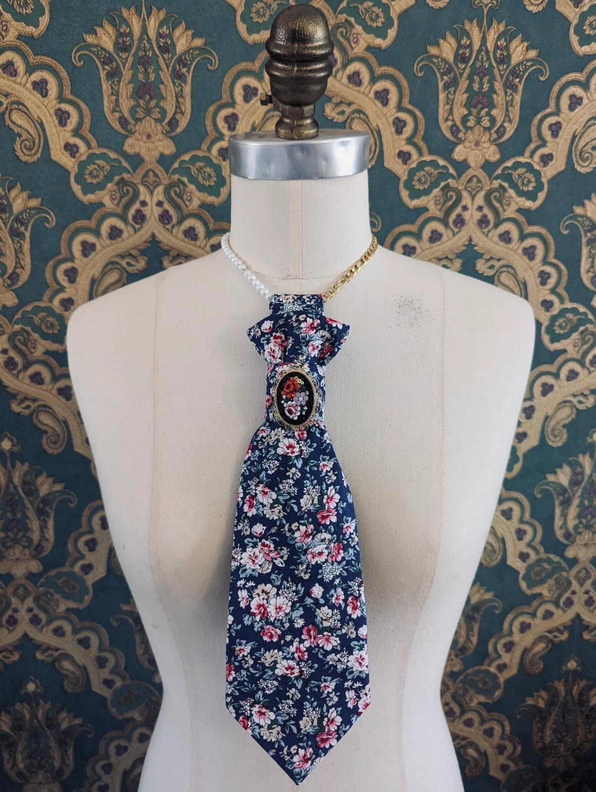 Broochella montecristo cravatta 11 navy floral, vintage, handmade, upcycled tie brooch, with vintage brooch embellishment. Pictured on a mannequin. The background is green and gold damask wallpaper.